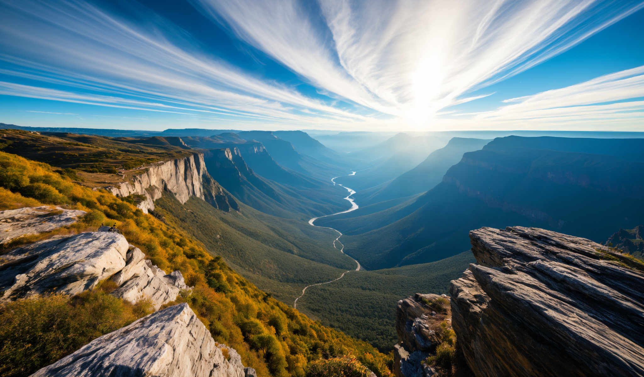 A breathtaking view of a valley with a winding river surrounded by mountains. The river appearing like a silver ribbon meanders through the heart of the valley reflecting the sunlight. The mountains painted in shades of green and brown rise majestically on either side of the river their peaks reaching towards the clear blue sky. The sun shines brightly casting a warm glow over the entire scene. The image captures the serene beauty of nature in its raw form.