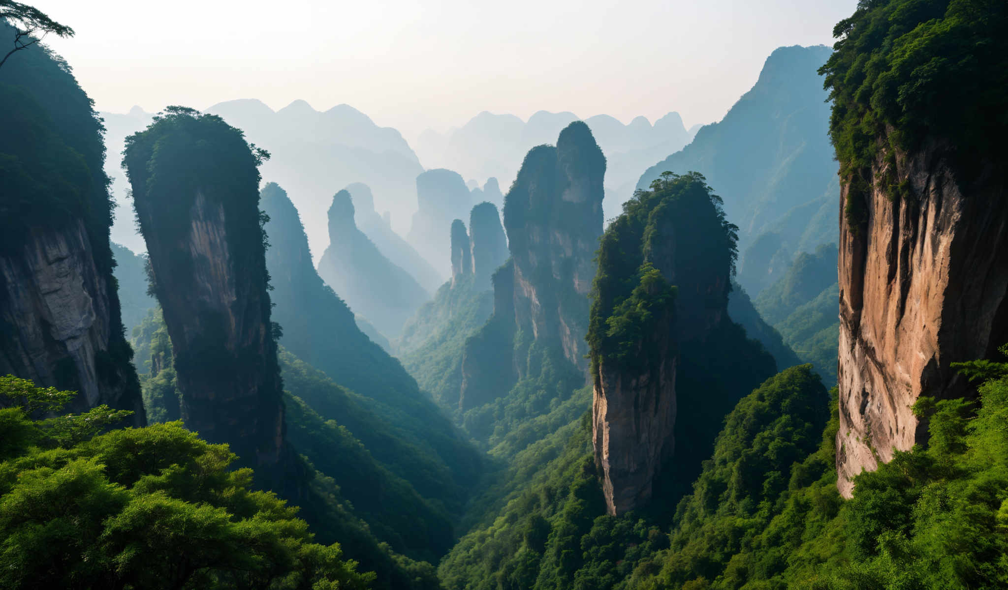 A breathtaking view of a mountainous landscape with a valley in the center. The mountains are covered in lush greenery and the sky is hazy. The image is taken from a high vantage point providing a panoramic view of the valley below. The colors in the image are predominantly green and blue with some brown and gray accents. The overall scene is serene and tranquil with the mountains standing tall and majestic. The valley in between the mountains is a beautiful sight with a river meandering through it. The sky above is hazing adding a sense of mystery to the scene. The high vocation point from which the photo is taken gives a sense scale and grandeur to the landscape. The greenery on the mountains and the valley gives a vibrant and lively feel to the image while the blue of the sky and the river adds a calming effect. The brown and grey accents on the rocks and the mountains add a touch of ruggedness to the otherwise peaceful scene. Overall the image is a stunning representation of nature's beauty and grand scale.