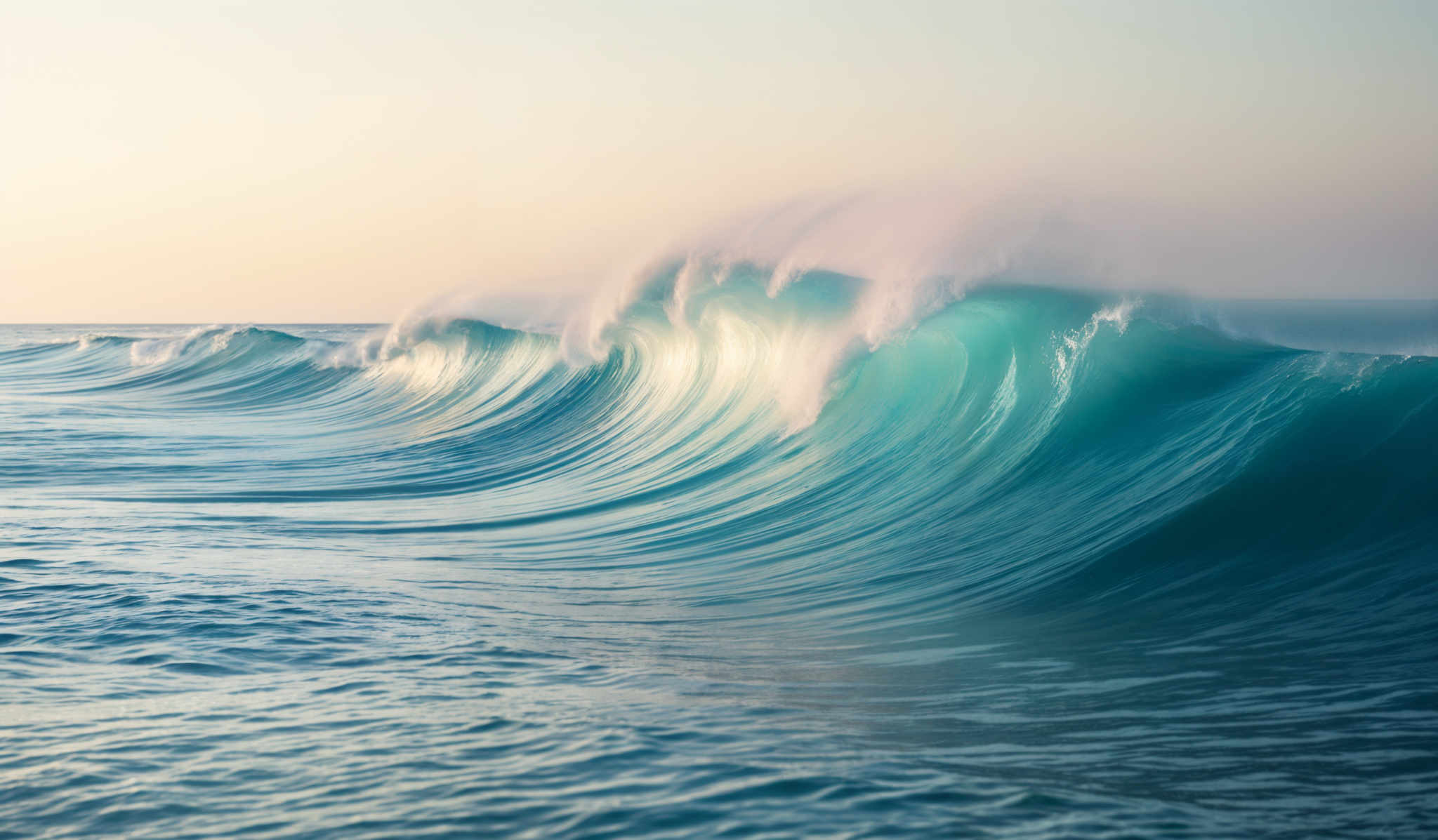 The image showcases a beautiful seascape with a large, powerful wave crashing. The wave is a vibrant shade of turquoise, with white foam at its crest. The sunlight reflects off the wave, creating a shimmering effect. The sky above is a gradient of soft hues, transitioning from a pale blue to a warm golden-orange, suggesting either dawn or dusk. The horizon is visible in the distance, and the calm sea stretches out beyond the wave.