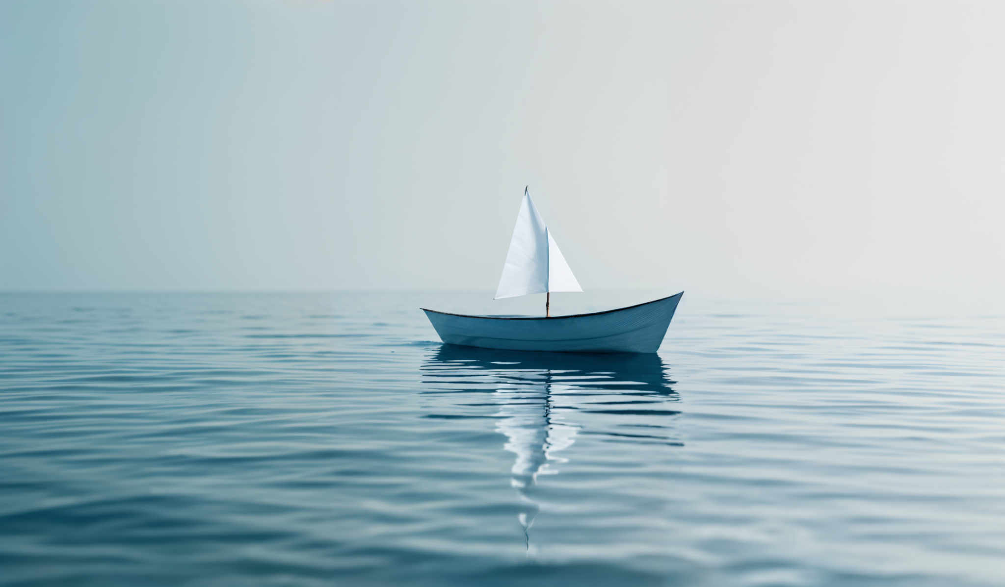 The image showcases a serene scene of a vast expanse of calm water. Dominating the center is a small sailboat with a triangular sail, gliding smoothly over the water's surface. The boat is painted in a light blue hue, which harmoniously blends with the surrounding water, creating a tranquil ambiance. The sky above is a soft gradient of light blue, fading into the horizon, suggesting either early morning or late afternoon. The reflection of the boat and the sky can be seen on the water, adding depth and symmetry to the composition.