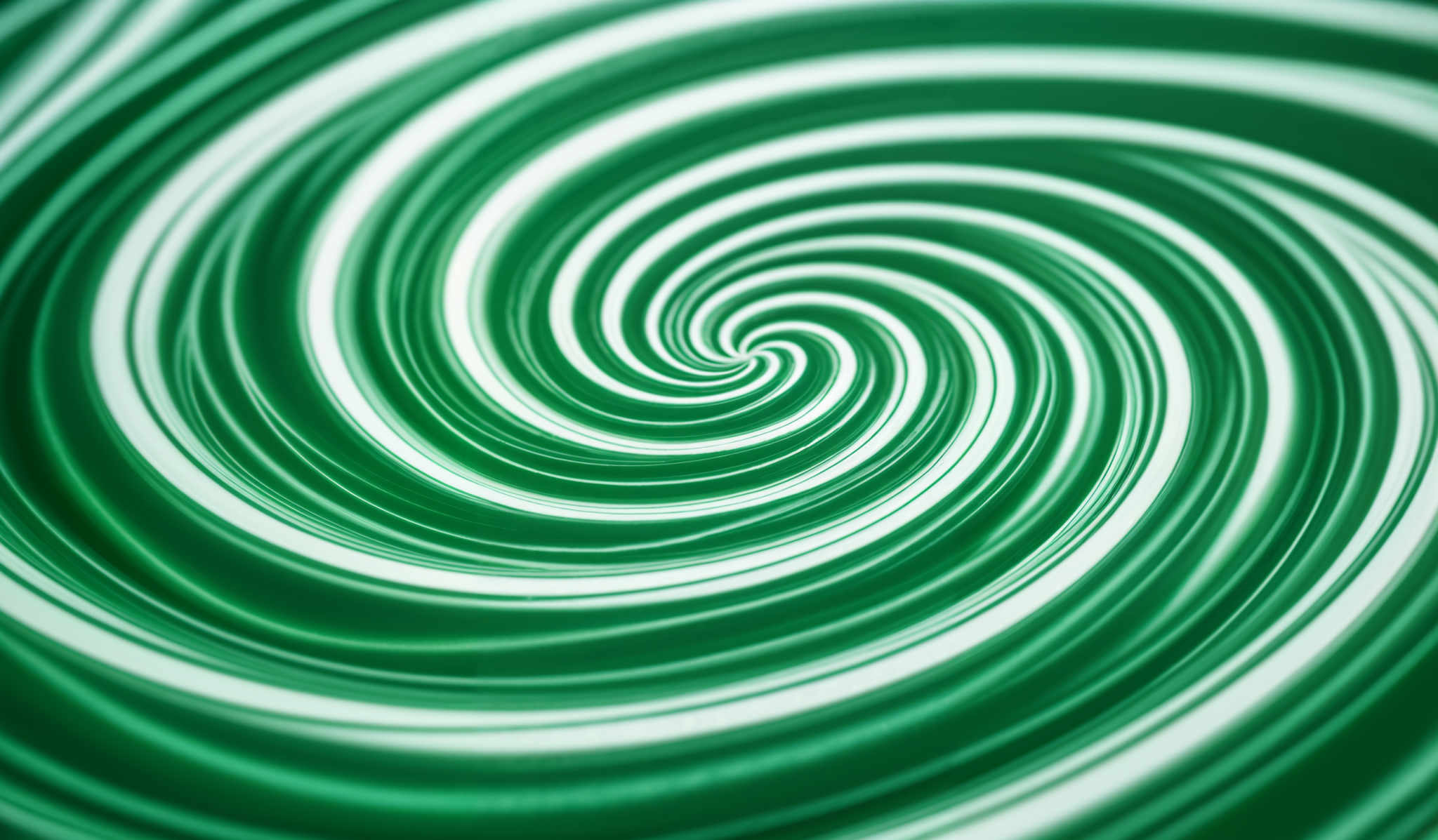 The image showcases a swirling pattern with varying shades of green. The swirl starts from a central point and spirals outwards, creating a hypnotic effect. The colors transition from a darker shade at the center to a lighter shade towards the edges. The intricate details and smooth gradients give the image a dynamic and mesmerizing appearance.