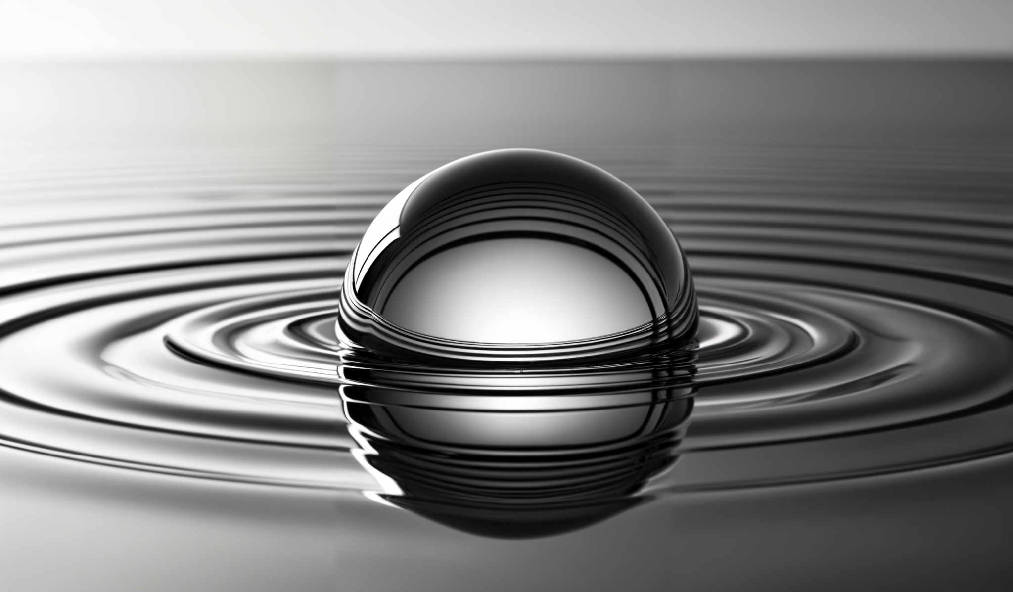 The image showcases a spherical object, possibly a crystal or a glass ball, submerged in a liquid. The liquid appears to be in motion, creating concentric ripples around the object. The color palette is predominantly monochromatic, with shades of black, white, and gray, giving the image a stark and dramatic appearance.