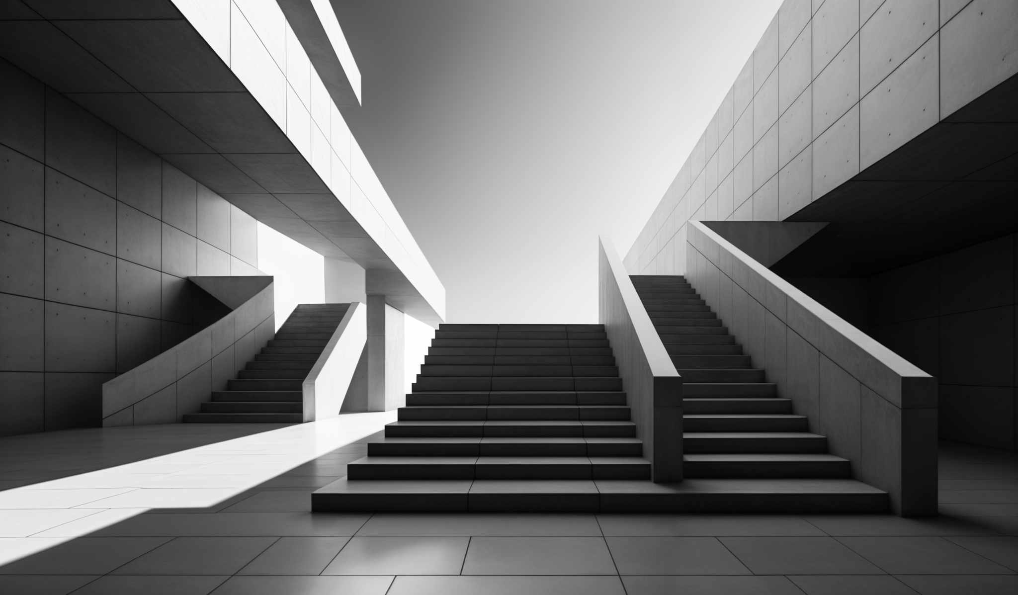 The image showcases a monochromatic architectural setting, predominantly in shades of gray. The primary focus is on a series of staircases, each with a distinct geometric design. The staircase on the left is a straight flight, while the one on the right has a more angular, zigzag design. Both stairways are flanked by large, rectangular walls with a uniform pattern of small rectangular openings. The floor is tiled, reflecting the light from the top, creating a play of shadows and light throughout the space.