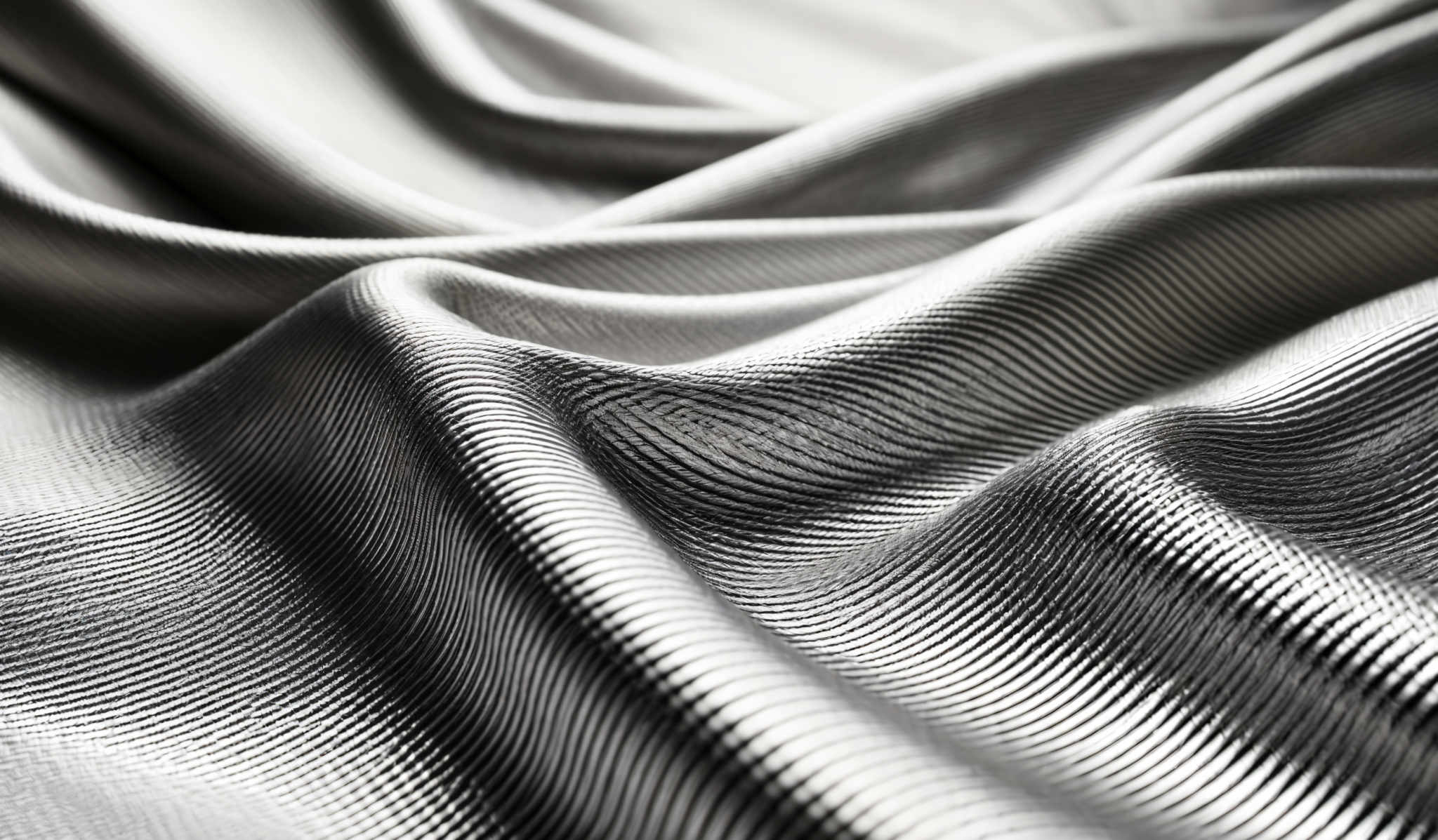 The image showcases a close-up view of a textured fabric with a metallic sheen. The predominant colors are shades of silver and gray, with intricate patterns of ridges and waves. The fabric appears to be folded or draped, creating multiple layers and curves, which add depth and dimension to the image, making it visually captivating.