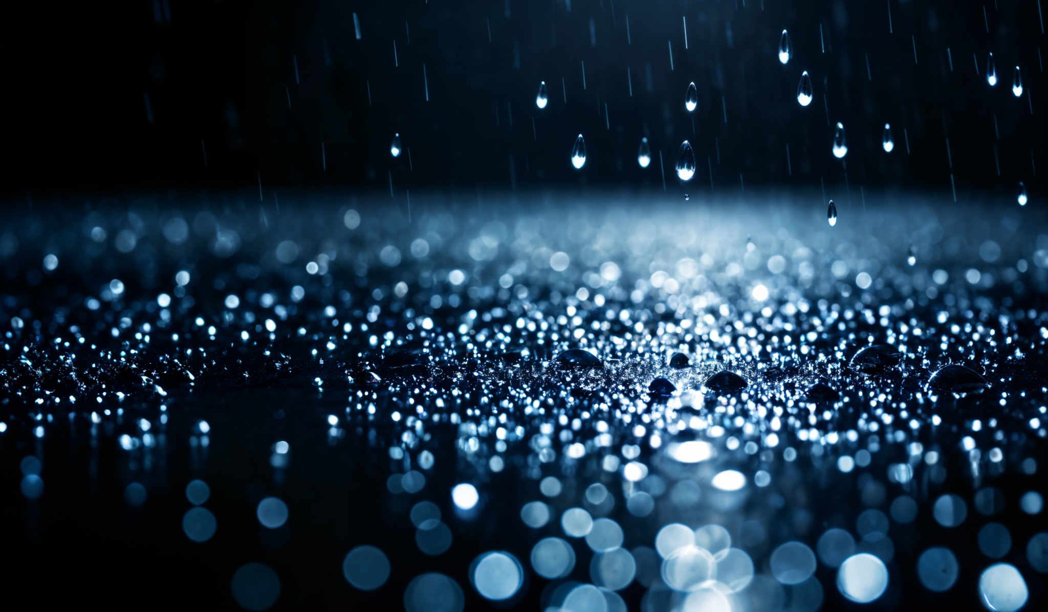 The image showcases a mesmerizing scene of droplets of water, possibly rain or dew, against a dark background. The droplet shapes vary from elongated to round, reflecting light in various hues of blue and white. The entire scene is illuminated, giving the droplettes a sparkling appearance, reminiscent of a starry night or a galaxy.