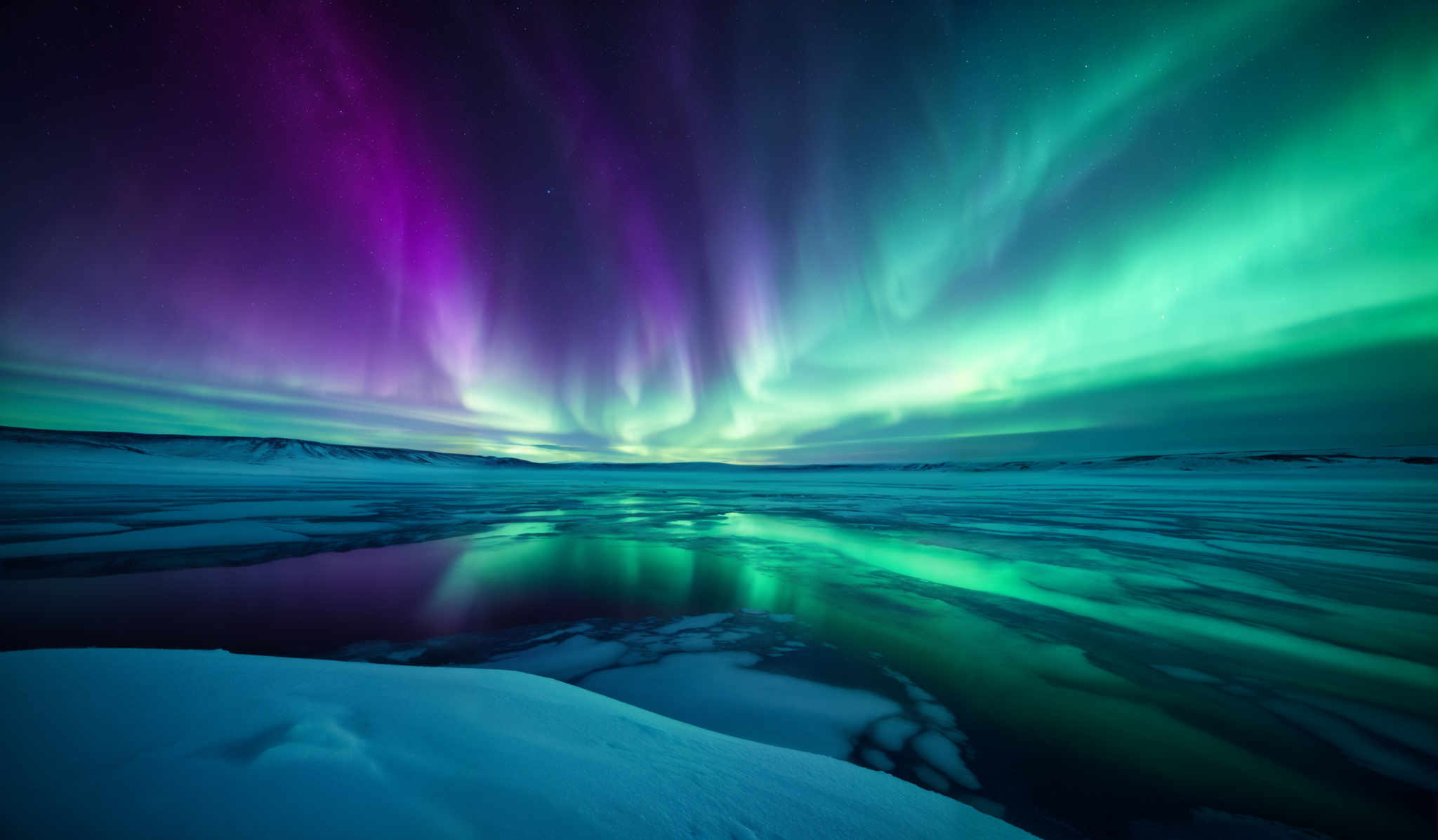 The image showcases a breathtaking view of the Northern Lights, also known as the Aurora Borealis. The colors range from deep purples and blues to vibrant greens and teals. The lights display a swirling pattern, creating an ethereal dance across the night sky. Below, there's a frozen landscape with patches of ice and water reflecting the colors of the sky. The horizon reveals a distant landform, possibly a coastline or a series of hills.