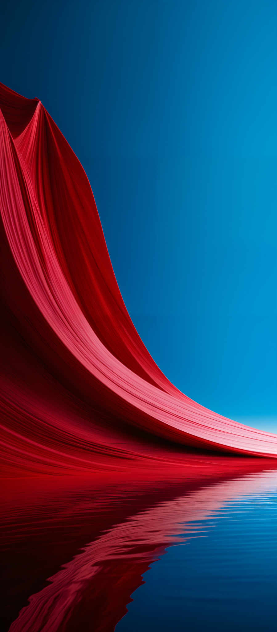 The image showcases a striking contrast between vibrant red and deep blue. The red forms a flowing, wave-like structure that appears to be cascading downwards, reminiscent of a draped fabric or a waterfall. This red structure is reflected perfectly in a calm body of water below, creating a mirror image. The blue background provides a stark contrast to the red, emphasizing its vibrancy. The overall composition gives a sense of movement and fluidity.