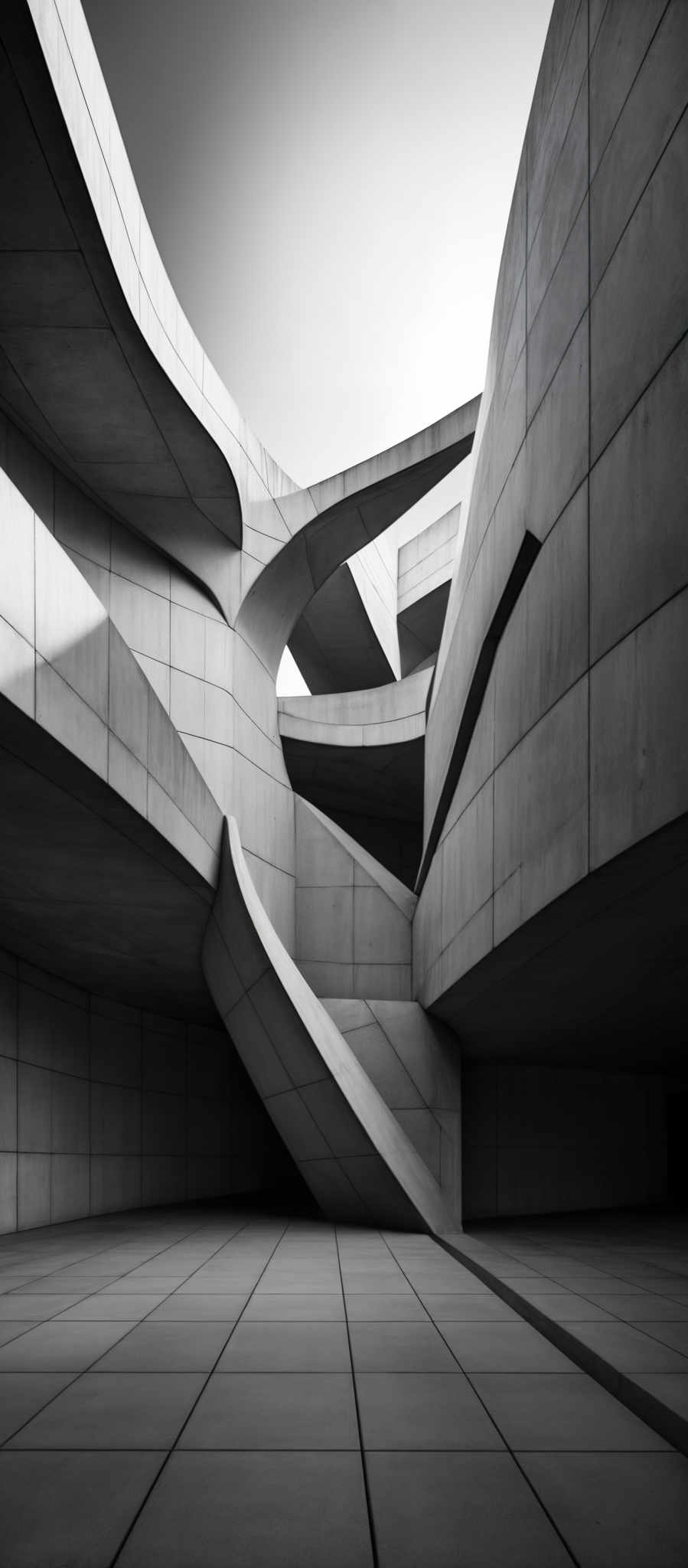 The image showcases a monochromatic architectural structure. The predominant colors are shades of gray, ranging from light to dark. The structure features curvilinear and fluid shapes, reminiscent of organic forms, but with a modern and geometric twist. The building appears to be made of concrete or a similar material, with large panels and smooth surfaces. The design is intricate, with overlapping arches and tunnels creating a labyrinth-like effect. The floor is tiled, and the overall ambiance is one of modern architectural elegance.