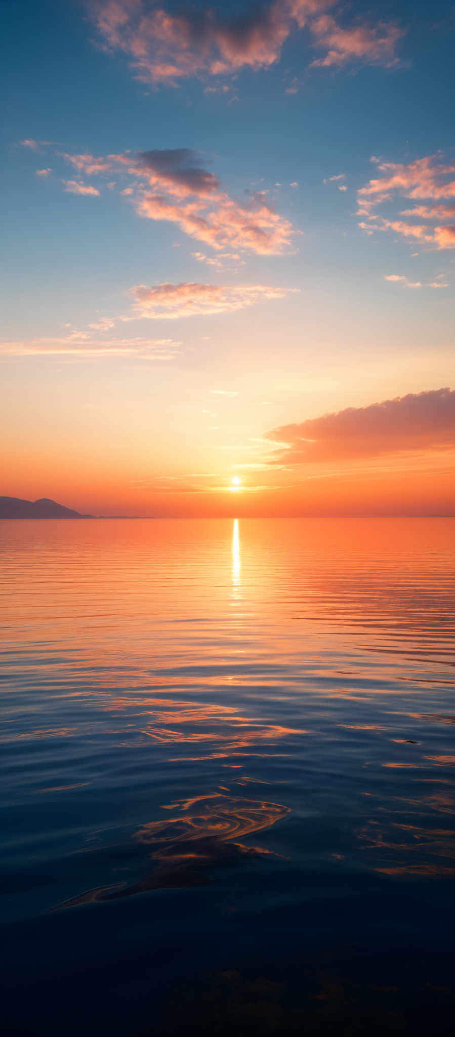 The image showcases a serene sunset over a calm body of water. The sky is painted with hues of blue, transitioning to a golden-orange near the horizon. The sun is captured just above the waterline, casting a brilliant reflection on the water's surface. The clouds are scattered, with some appearing fluffy and others more wispy, reflecting the sun's colors. The water has gentle ripples, creating a shimmering effect as it mirrors the sky's beauty.