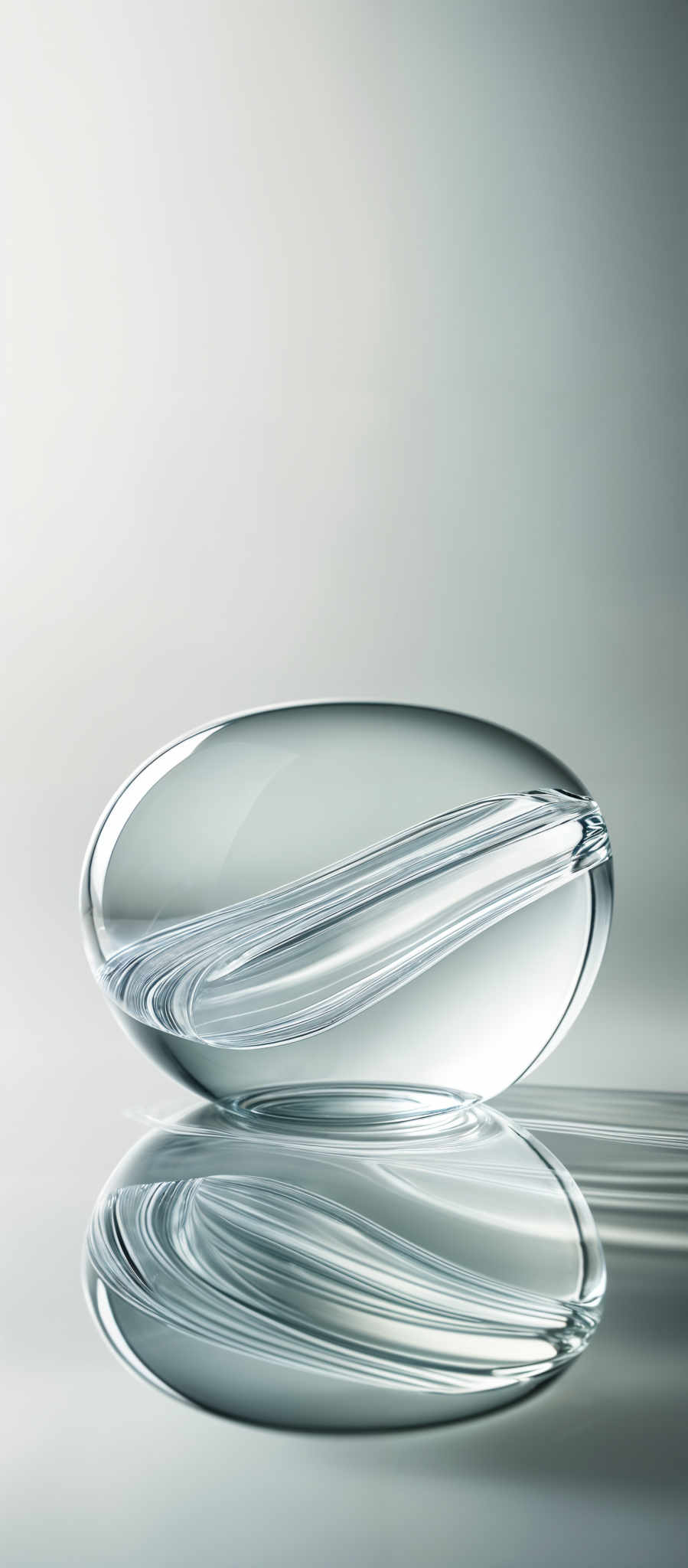 The image showcases a clear, oval-shaped object, possibly made of glass or crystal, that appears to be suspended in mid-air. The object has intricate swirls and patterns within it, giving it a unique and artistic appearance. The background is a gradient of light gray, creating a serene and minimalistic ambiance. The reflection of the object can be seen on the surface below, adding depth and dimension to the image, and the overall color palette is dominated by cool and neutral tones.