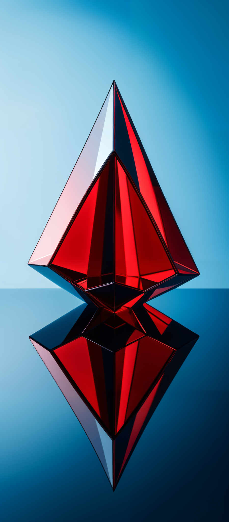 The image showcases a three-dimensional geometric object that resembles a pyramid or a prism. It is split into two distinct colors: a vibrant red on the top and a deep blue on the bottom. The object is positioned against a gradient background that transitions from a light blue at the top to a darker blue at its base. The reflection of the object can be seen on a smooth surface below, creating a mirror image.