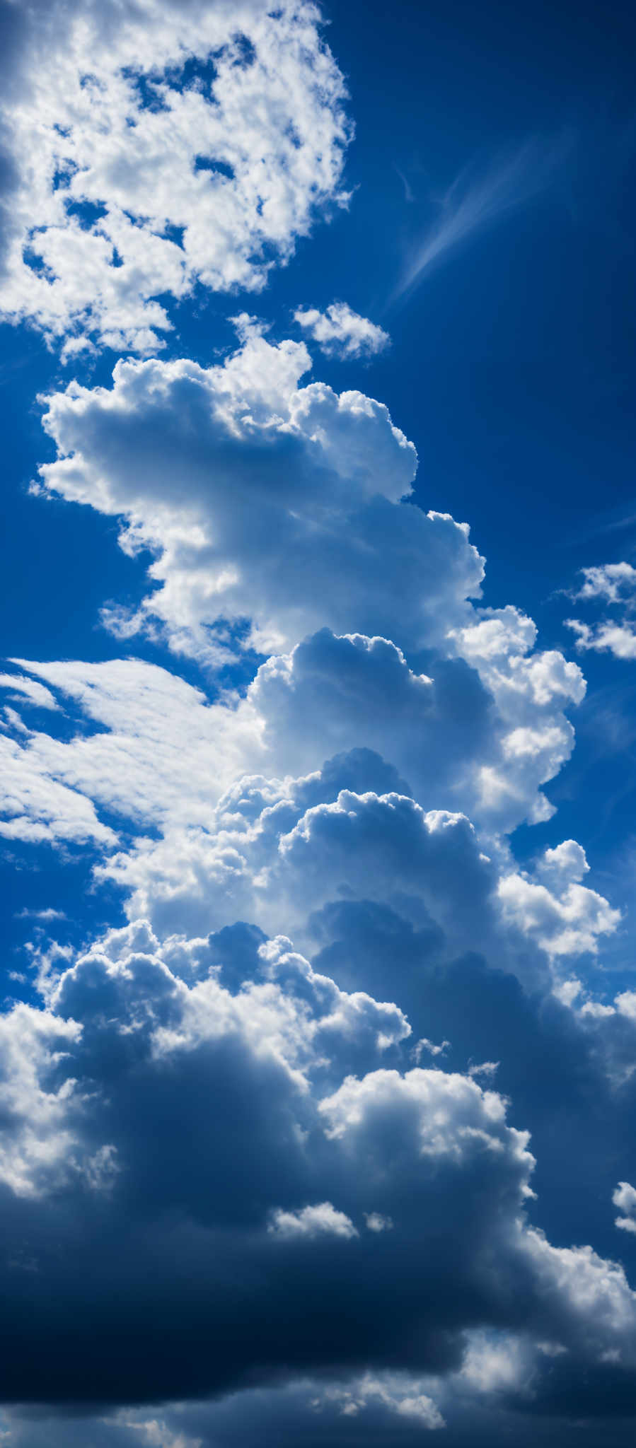 The image showcases a vast expanse of the sky, dominated by a deep blue hue. The sky is dotted with fluffy white clouds, varying in size and shape. Some clouds appear dense and billowing, while others are more sparse. The play of light and shadow on the clouds gives depth and dimension to the scene. The overall atmosphere evokes a sense of serenity and vastness.