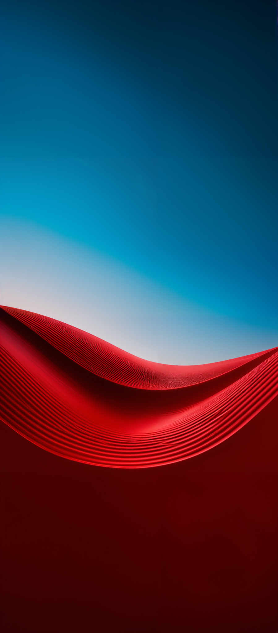 The image showcases a striking contrast between deep red and vibrant blue. The foreground is dominated by a series of undulating red sand dunes, exhibiting a smooth texture with ripples created by wind patterns. These dunes are set against a clear blue sky, which gradually fades from a deep blue at the top to a lighter shade near the horizon. The interplay of colors and shapes creates a visually captivating and serene landscape.