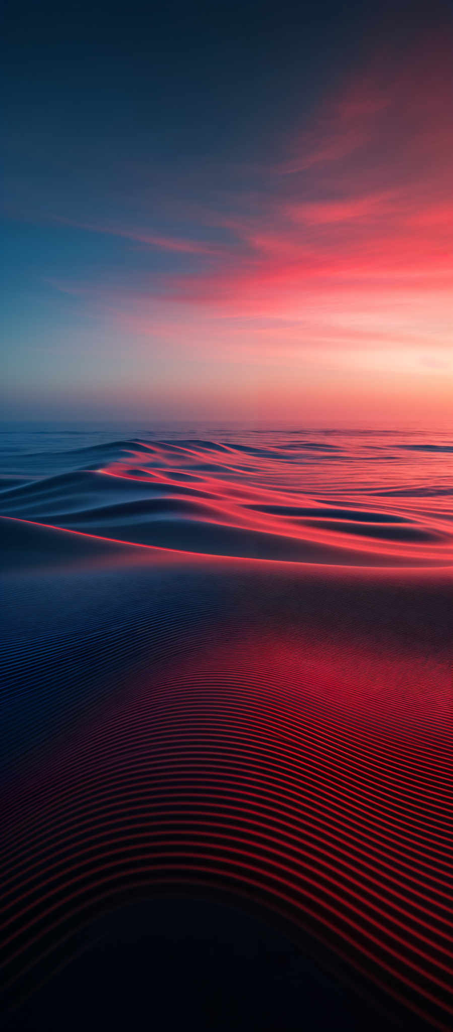 The image showcases a serene beach scene during sunset. The sky is painted with hues of deep blue transitioning to vibrant shades of pink and orange. The sun casts a warm, reddish glow on the sand dunes, creating a beautiful contrast with the darker shadows. The sand dune patterns are intricate, with ripples and waves formed by the wind, highlighting the texture and movement of the sand. The calm sea in the background reflects the colors of the sky, adding to the overall tranquility of the scene.