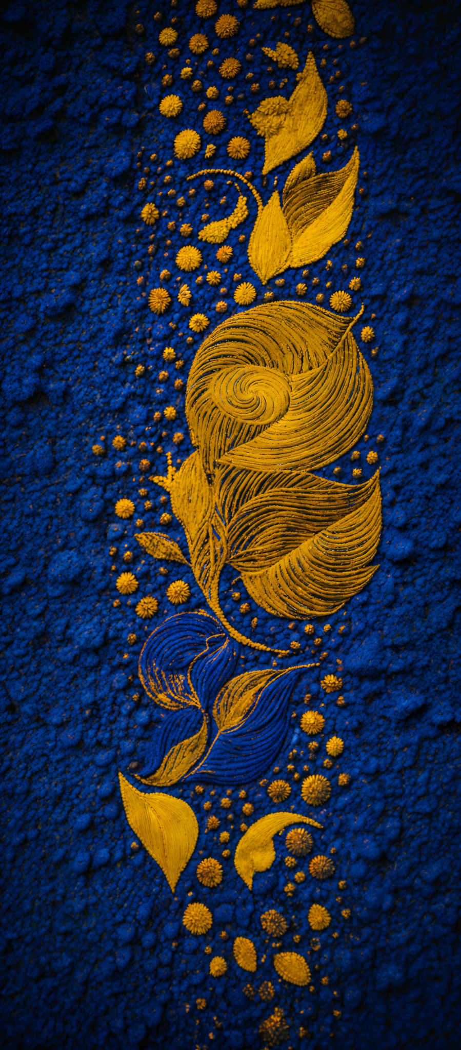 The image predominantly features a deep blue background with a textured, bumpy surface. On this background, there are intricate golden designs that resemble leaves and floral motifs. The golden designs are symmetrically arranged, with some overlapping others. The patterns are detailed, with the leaves having varying shapes and sizes, and the floral designs showcasing intricate swirls and curves.