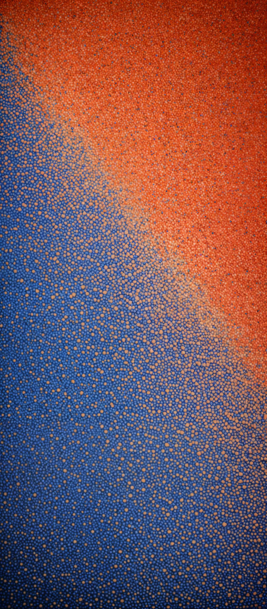 The image showcases a vibrant contrast between two textures. On the left side, there's a deep blue texture with a speckled appearance, resembling a grainy or granulated surface. On its right, there is a bright orange texture that looks like a coarse, grainy material, possibly sand or a similar substance. The two textured surfaces meet at a diagonal line, creating a sharp boundary between them.