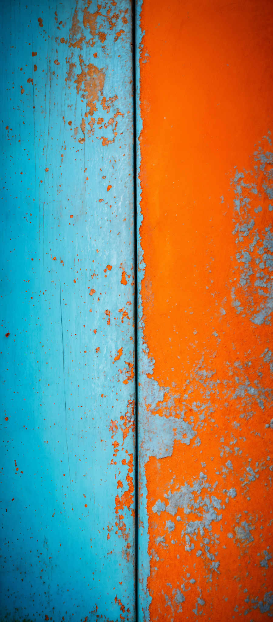 The image showcases two distinct colors side by side. On the left, there's a vibrant shade of blue with a worn-out appearance, characterized by chipped paint and visible brush strokes. The right side is a bright orange with similar signs of wear and tear, but the paint seems to be peeling off in larger patches. The juxtaposition of these two colors creates a striking contrast.