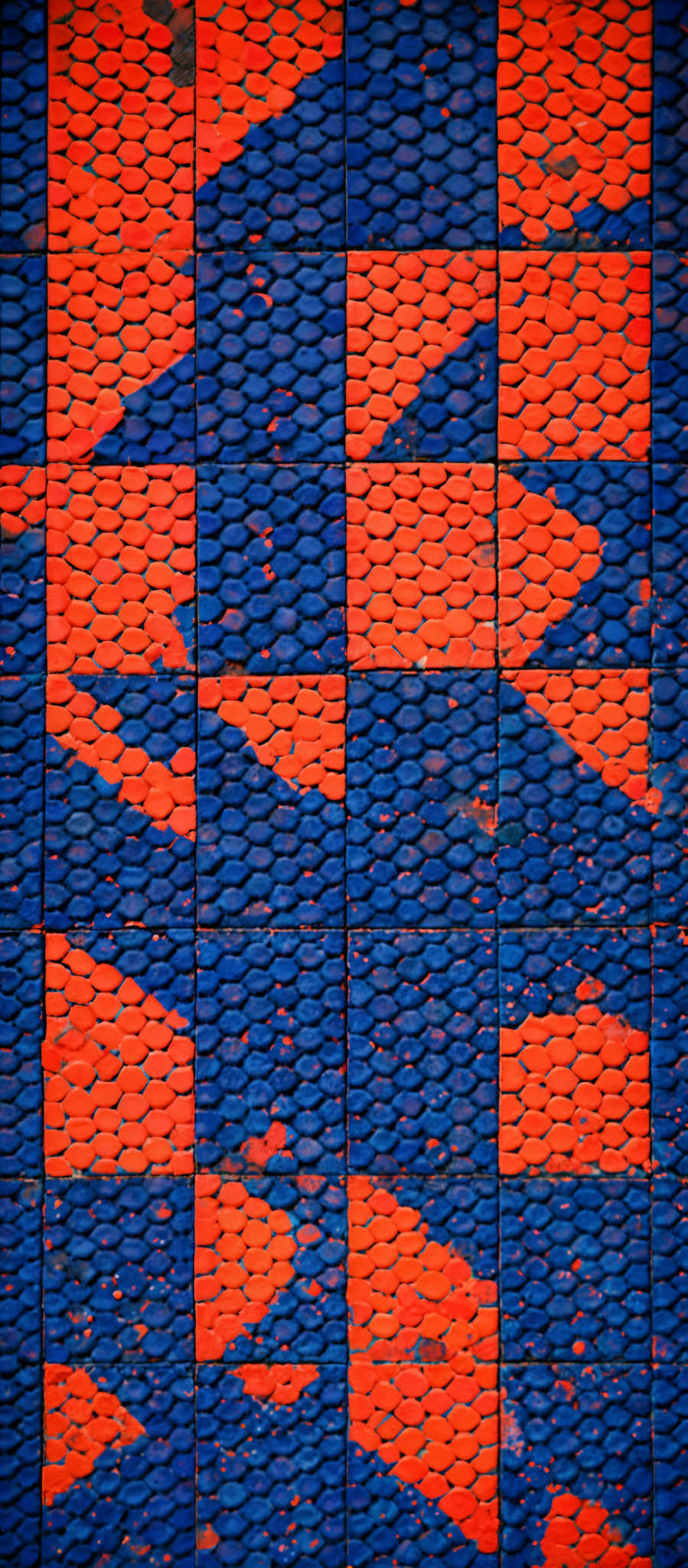 The image showcases a pattern of interlocking rectangular tiles. These tiles are divided into two primary colors: blue and orange. The blue tiles have a consistent, wavy pattern, while the orange tiles exhibit a more irregular, speckled pattern. The tiles seem to be arranged in a checkerboard-like manner, but the irregularities in the orange pattern disrupt the symmetry.