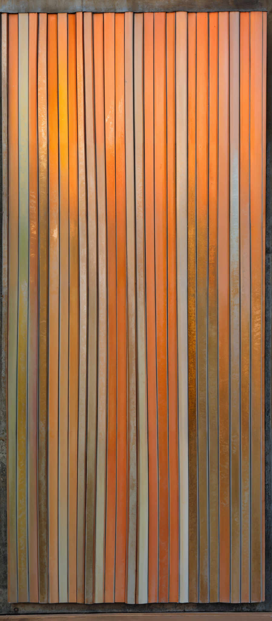 The image showcases vertical strips of varying colors and shades. The dominant colors are shades of orange, peach, and beige, with subtle variations in hue. The strips are evenly spaced and have a wavy, undulating appearance. The background is a darker shade, possibly a deep gray or black, which contrasts with the lighter strips, making them stand out prominently.