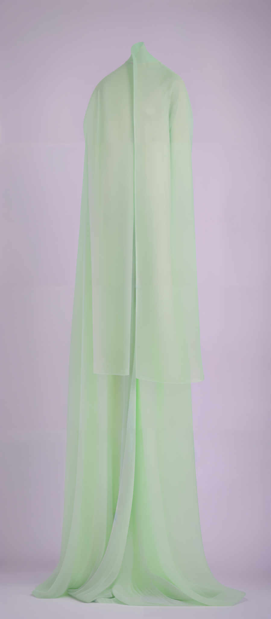 The image showcases a translucent, light green fabric draped over a mannequin. The fabric appears soft and flowy, cascading down in gentle folds. The mannequins head is obscured by the fabric, and only the back and shoulders are visible. The background is a muted purple, which contrasts with the vibrant green of the fabric.