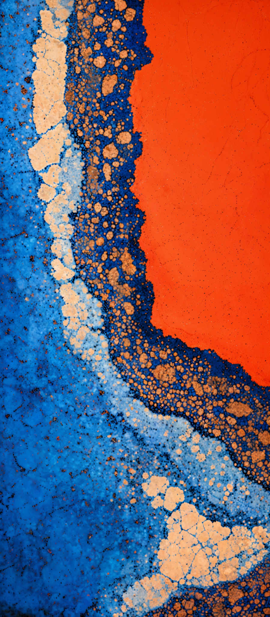 The image showcases a vibrant and abstract design. The dominant colors are blue and orange. The blue forms a wavy pattern, almost resembling ocean waves, with some areas having a cracked texture. The orange forms a sharp, rectangular boundary that contrasts with the blue. There are also white speckles scattered throughout, adding depth and texture to the design.