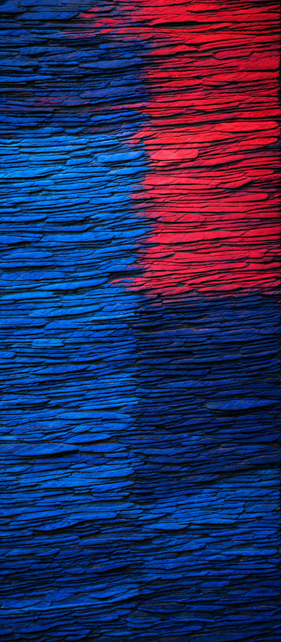 The image showcases a textured surface with horizontal lines. The predominant colors are shades of blue and red. The blue is a deep, rich hue, while the red is a vibrant, fiery shade. The texture appears to be that of stacked or layered materials, possibly resembling slate or stone. The lines are evenly spaced and run horizontally across the image, creating a sense of rhythm and pattern.