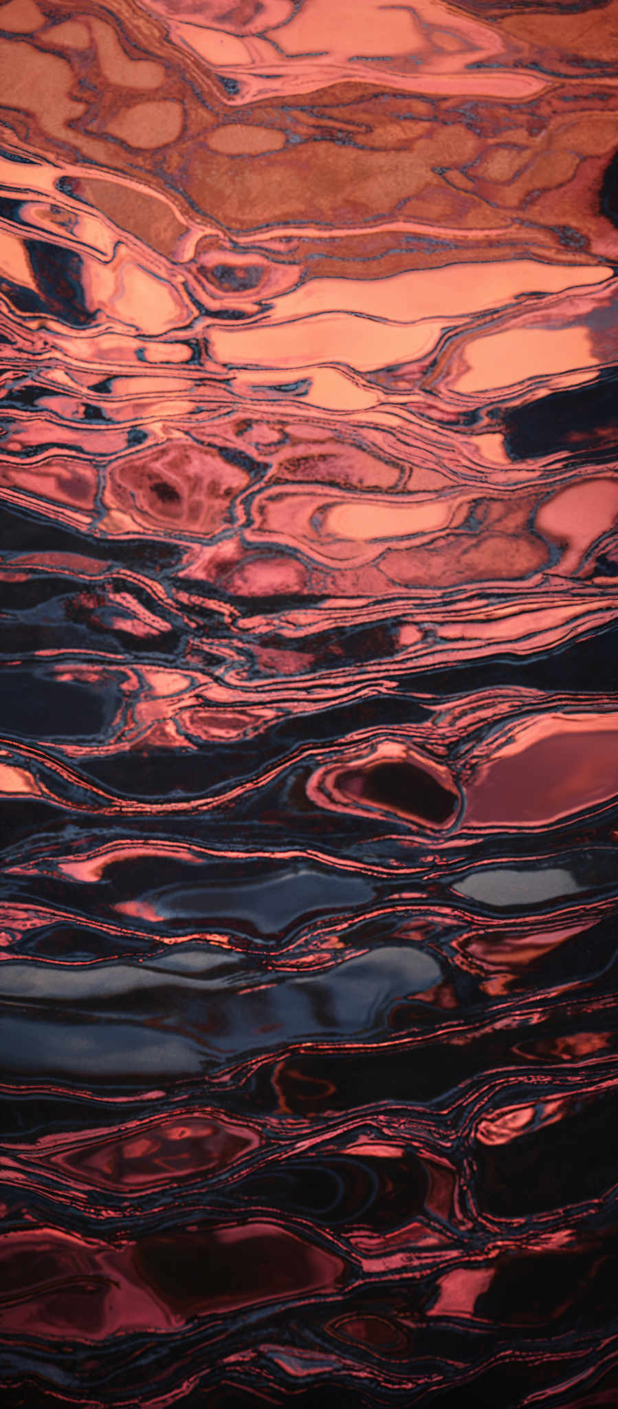 The image showcases a mesmerizing pattern of colors and shapes. It features a mix of deep blues, vibrant oranges, and rich reds, creating a visually captivating effect. The shapes resemble liquid patterns, reminiscent of oil or water, with wavy and flowing lines intertwining. The colors seem to be reflecting off of each other, creating an almost 3D effect.