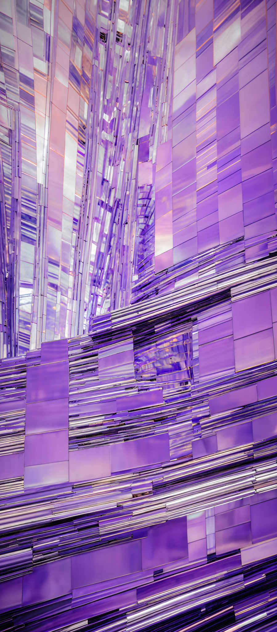 The image showcases a vibrant and intricate design with a plethora of colors. The dominant colors are shades of purple, blue, and pink, interspersed with hints of gold and silver. The design consists of layered rectangular and square blocks, some of which are transparent, allowing the underlying colors to shine through. The blocks are arranged in a manner that creates a sense of depth and movement, giving the impression of a dynamic, shimmering surface.