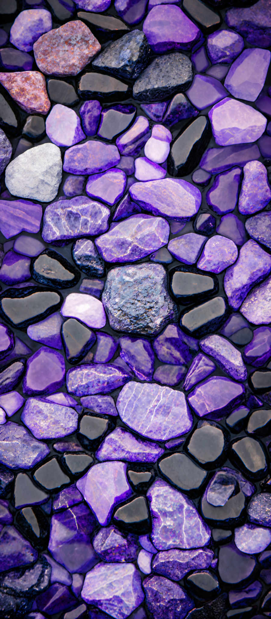 The image showcases a collection of rounded stones of various sizes and colors. The predominant colors are shades of purple, blue, and black. The stones are arranged in a manner that creates a mosaic-like pattern, with some stones having a glossy finish, possibly due to being wet or polished.