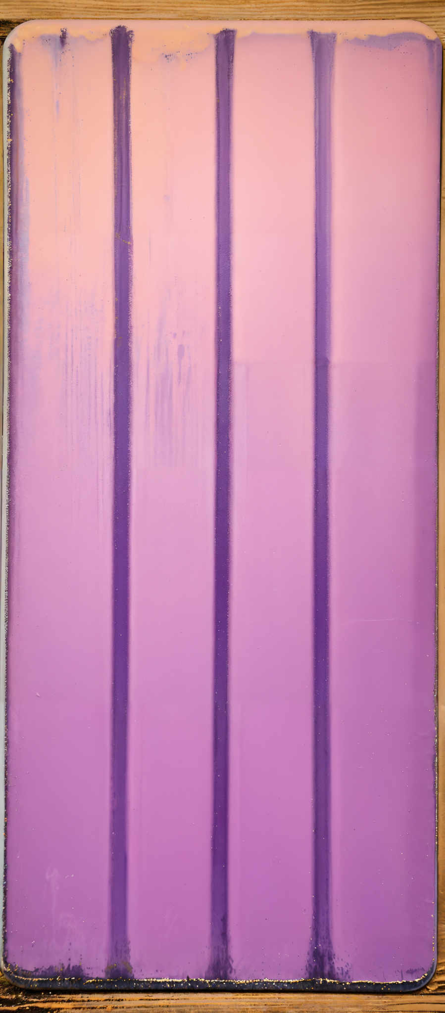 The image showcases a rectangular object with vertical lines. The primary color of the object is a shade of purple. The lines are evenly spaced and appear to be painted or printed on the purple surface. The edges of the image show signs of wear, with some chipping and discoloration, suggesting that the object might be old or has been exposed to external elements.