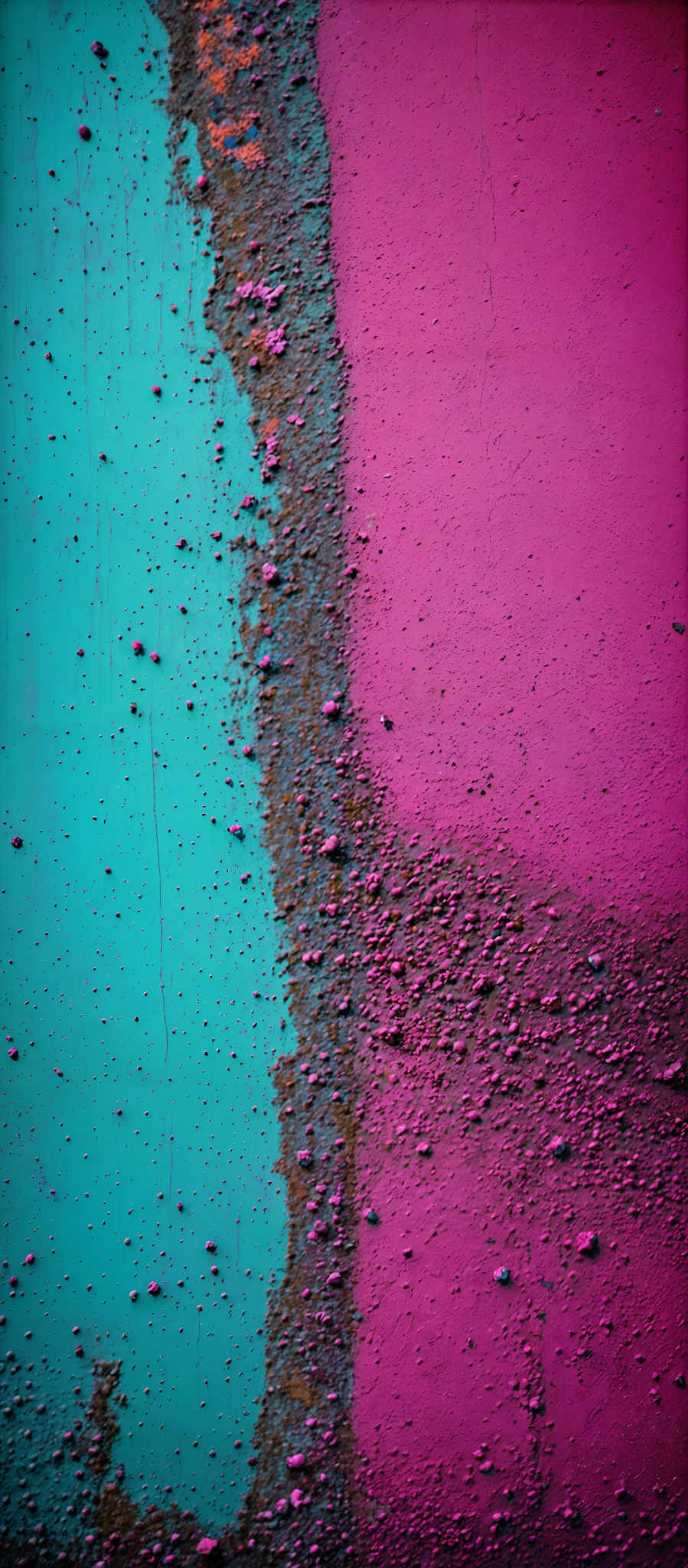 The image showcases a vibrant contrast between two primary colors: turquoise and pink. The turquois side has a rough texture with scattered specks and streaks, while the pink side appears smoother with a few scattered speckles. The boundary between the two colors is marked by a rough, uneven transition.