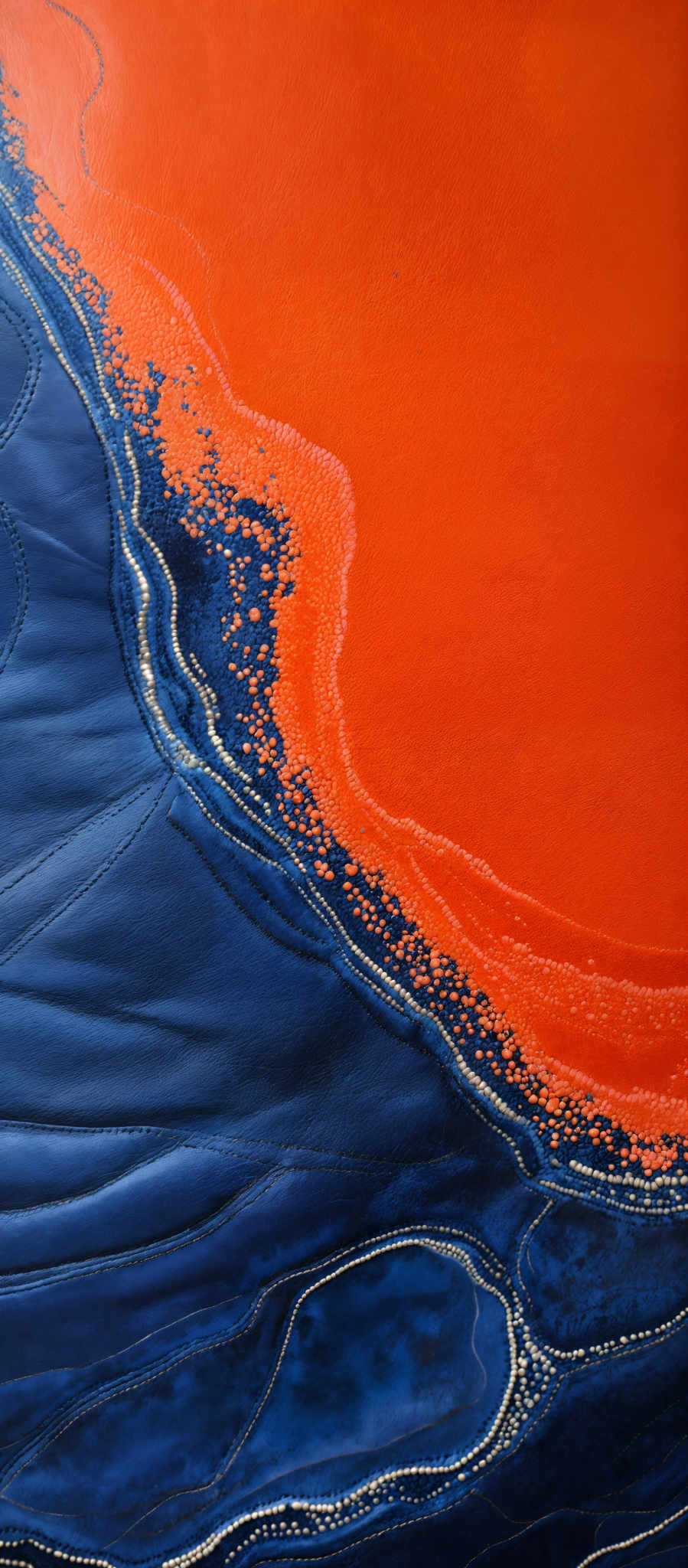 The image showcases a vibrant mix of colors. The dominant color is a deep shade of blue, which forms intricate patterns resembling waves or ripples. Adjacent to this blue, there's a striking orange hue that appears to be a contrasting element, possibly representing a different substance or layer. The orange color is more uniform and forms a border-like structure around the blue patterns. The overall composition gives an impression of a top-down view of a fluid or liquid, with the blue possibly representing water and the orange indicating a different medium or substance.