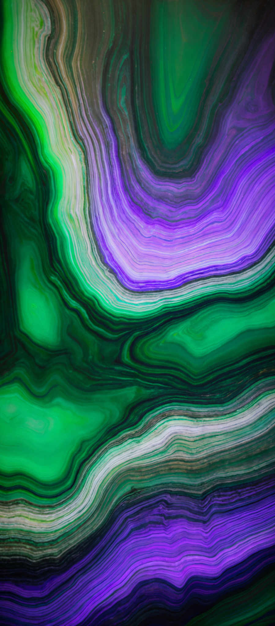 The image showcases a vibrant and intricate pattern of swirling colors. The dominant colors are shades of green, purple, and a hint of brown. The swirls are layered and seem to flow seamlessly, creating a marbled or agate-like appearance. The patterns are reminiscent of fluid dynamics or the natural formation of minerals.