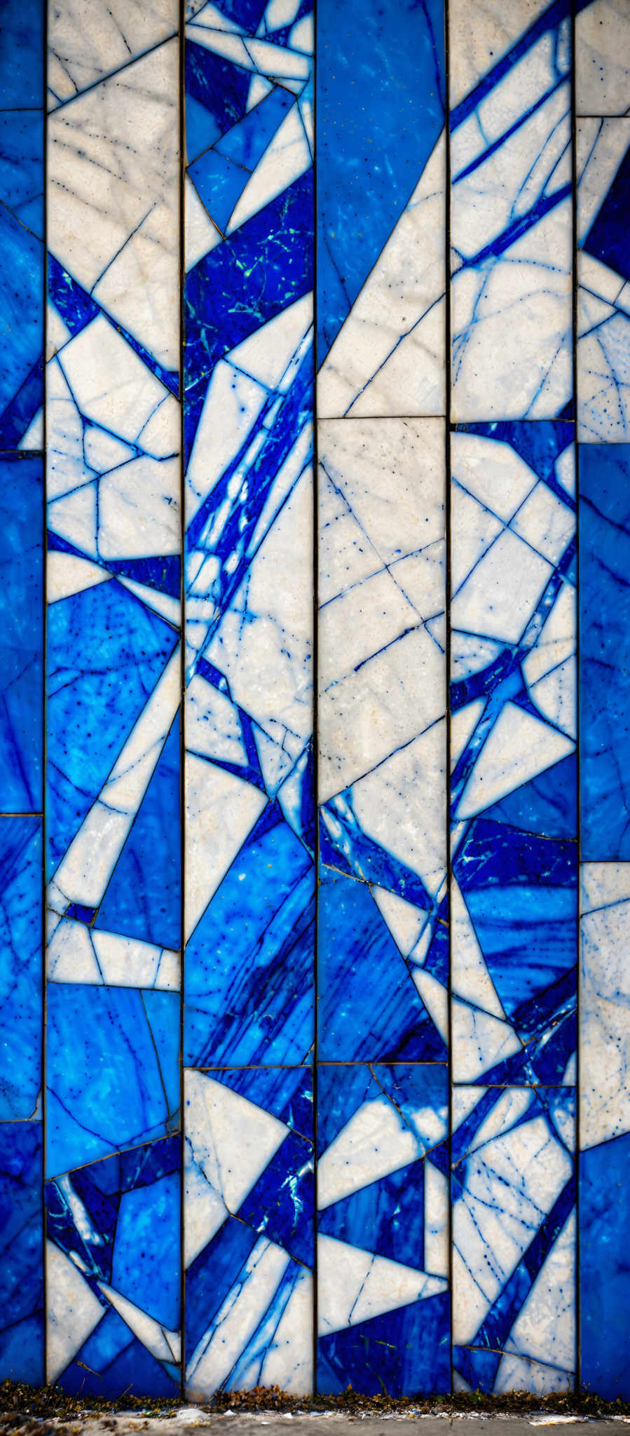 The image showcases a series of rectangular panels arranged vertically. Each panel is divided into two sections by a diagonal line. The left section is a solid blue color, while the right section has a white background with intricate blue patterns resembling cracks or veins. The patterns on the white section have a marbled appearance, with varying shades of blue and some speckled details.