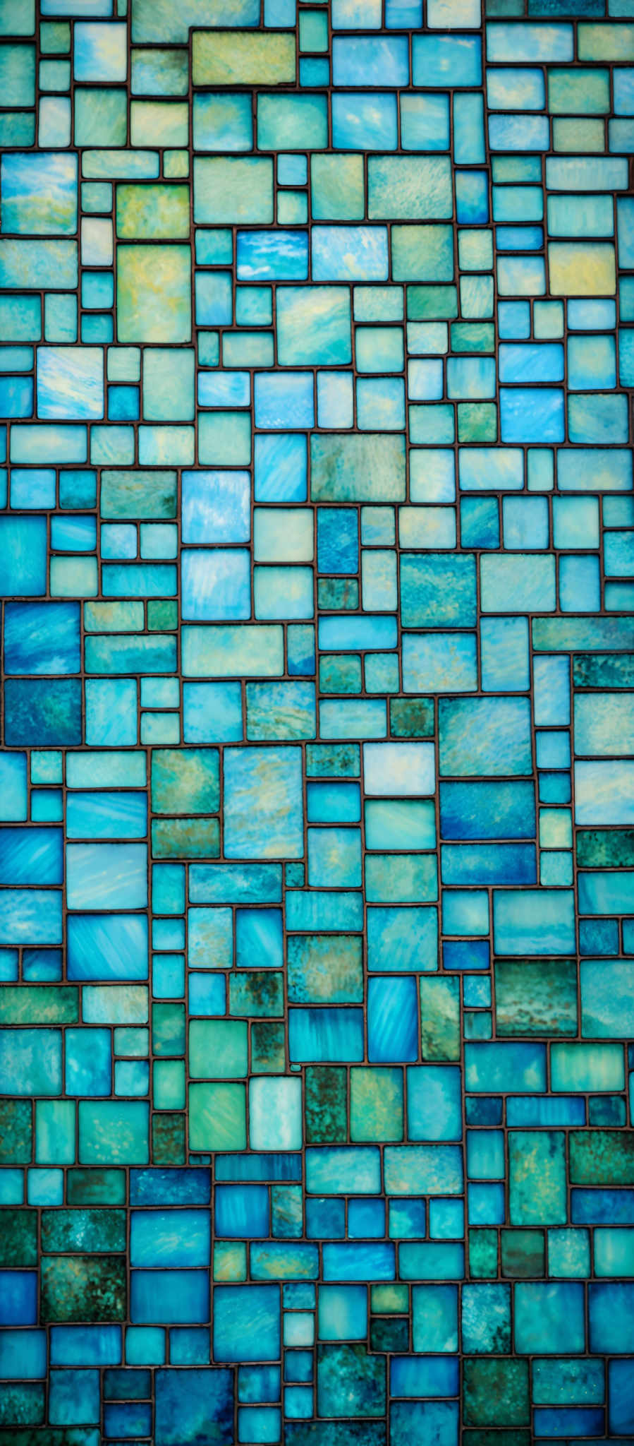 The image showcases a mosaic of various shades of blue, ranging from light turquoise to deep navy. The mosaics are arranged in a grid pattern, with each tile having a unique texture and pattern. Some tiles have a smooth finish, while others have a more marbled or swirled appearance. The overall effect is reminiscent of stained glass or watercolor paint splashed onto a canvas.