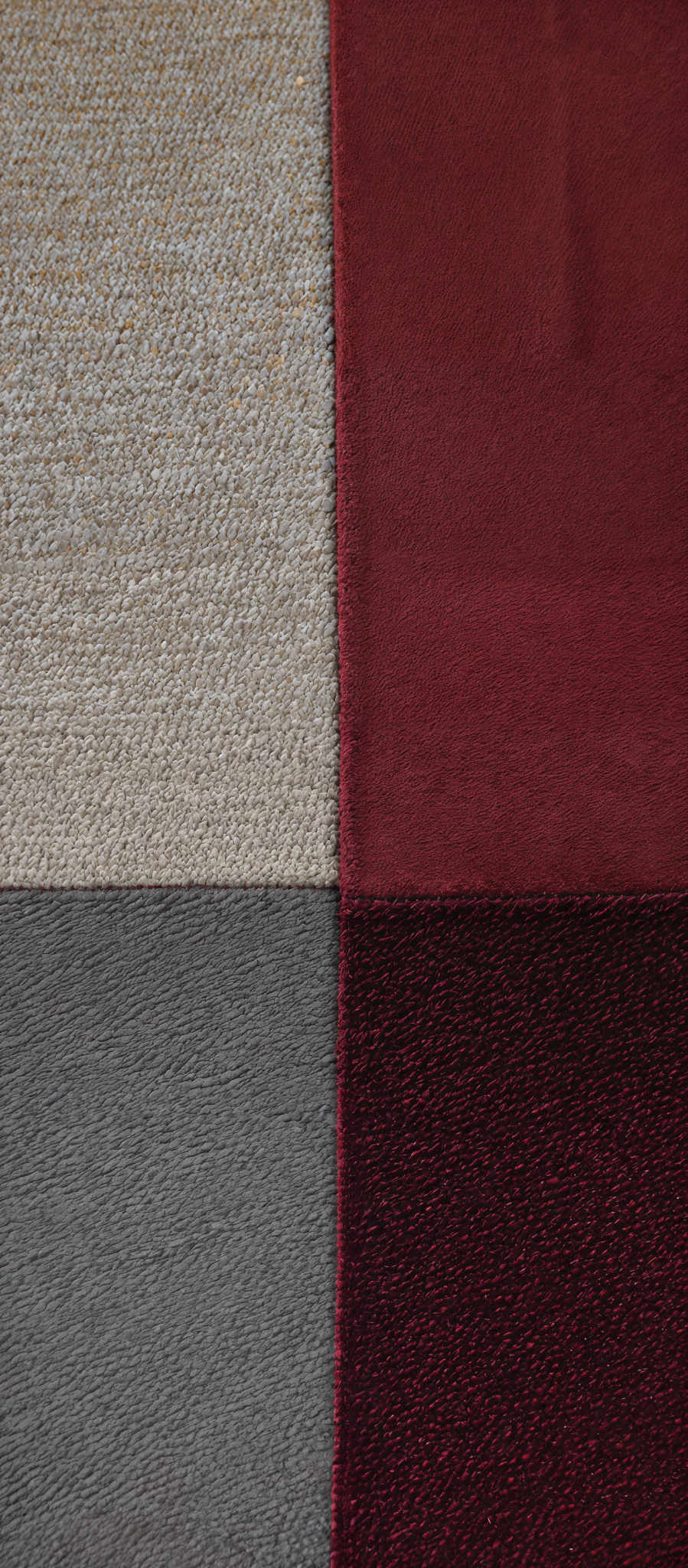 The image displays a rectangular section divided into four equal quadrants. The top-left quadrant has a light beige or off-white texture, resembling a woven or knitted fabric. The adjacent top-right quadrant is a deep red with a slightly glossy finish, possibly a velvet or plush material. The bottom-left is a dark gray with a textured appearance, reminiscent of a woolen or tweed fabric. Lastly, the bottom-right is a similar dark gray but with a more subtle texture, possibly resembles a silk or satin material.