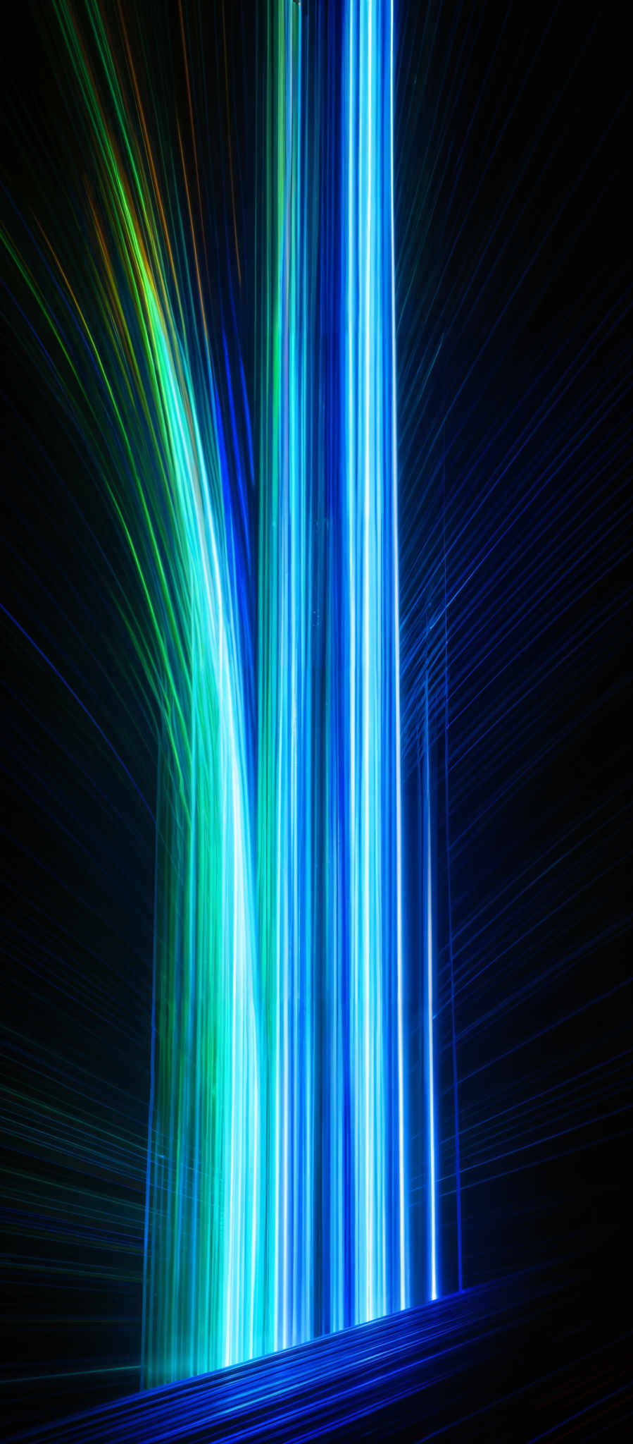 The image showcases a vibrant and dynamic visual of streaks of light. The colors range from deep blues to bright neon greens and yellows. The streaks appear to be moving in both vertical and horizontal directions, creating a sense of motion and energy. The overall shape is reminiscent of a cascading waterfall or a burst of energy emanating from a source.