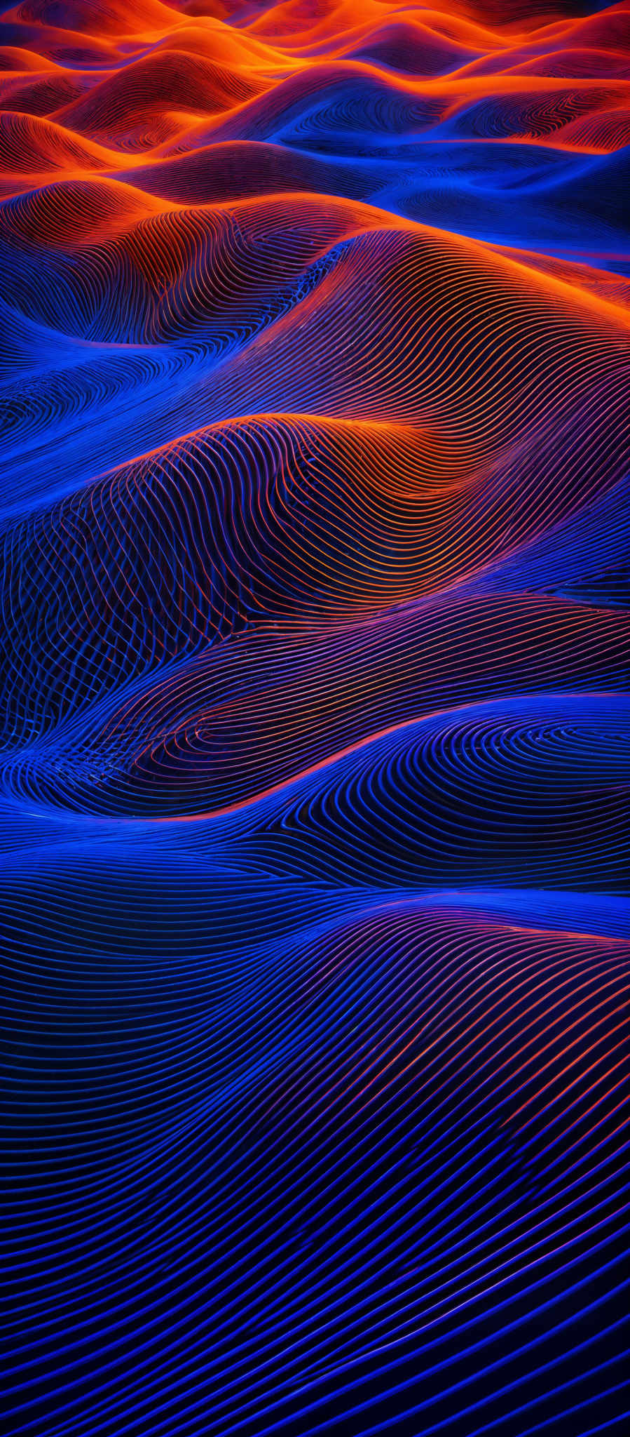 The image showcases a mesmerizing pattern of undulating sand dunes. The dunes are highlighted with a vibrant interplay of blue and orange hues, creating a visually striking contrast. The intricate ripples and patterns on the dunes suggest the influence of wind over time, giving the dune formations a textured and organic appearance.