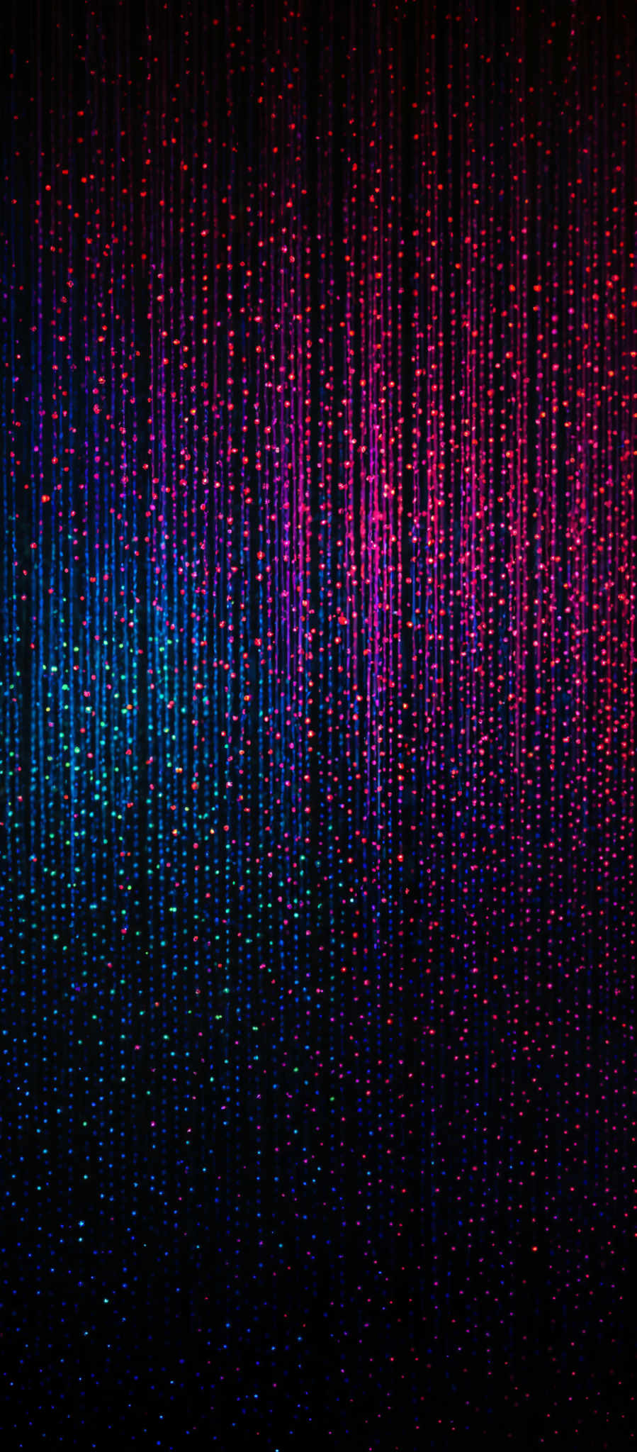 The image showcases a vibrant display of vertical streaks, each emitting a glowing light. The colors range from deep blue at the top to a gradient of pink, purple, and red towards the bottom. The streaks appear to be evenly spaced and are densely packed, creating a mesmerizing effect. The overall appearance is reminiscent of a digital rain or a visual representation of data being processed.