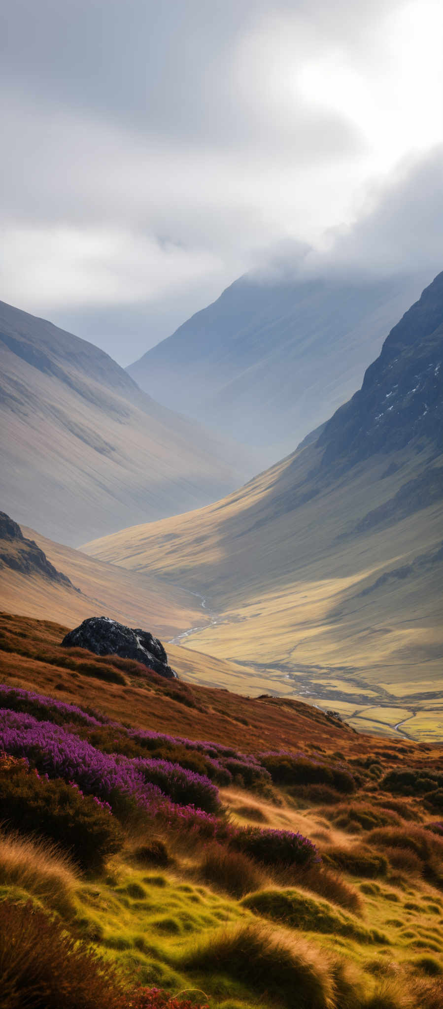 A breathtaking view of a mountainous landscape with a river meandering through it. The mountains are a mix of green and brown indicating a rich ecosystem. The river a lifeline in the wilderness is surrounded by a lush expanse of purple flowers. The sky above is a clear blue adding to the serene atmosphere. The image captures the beauty and tranquility of nature in its raw form.