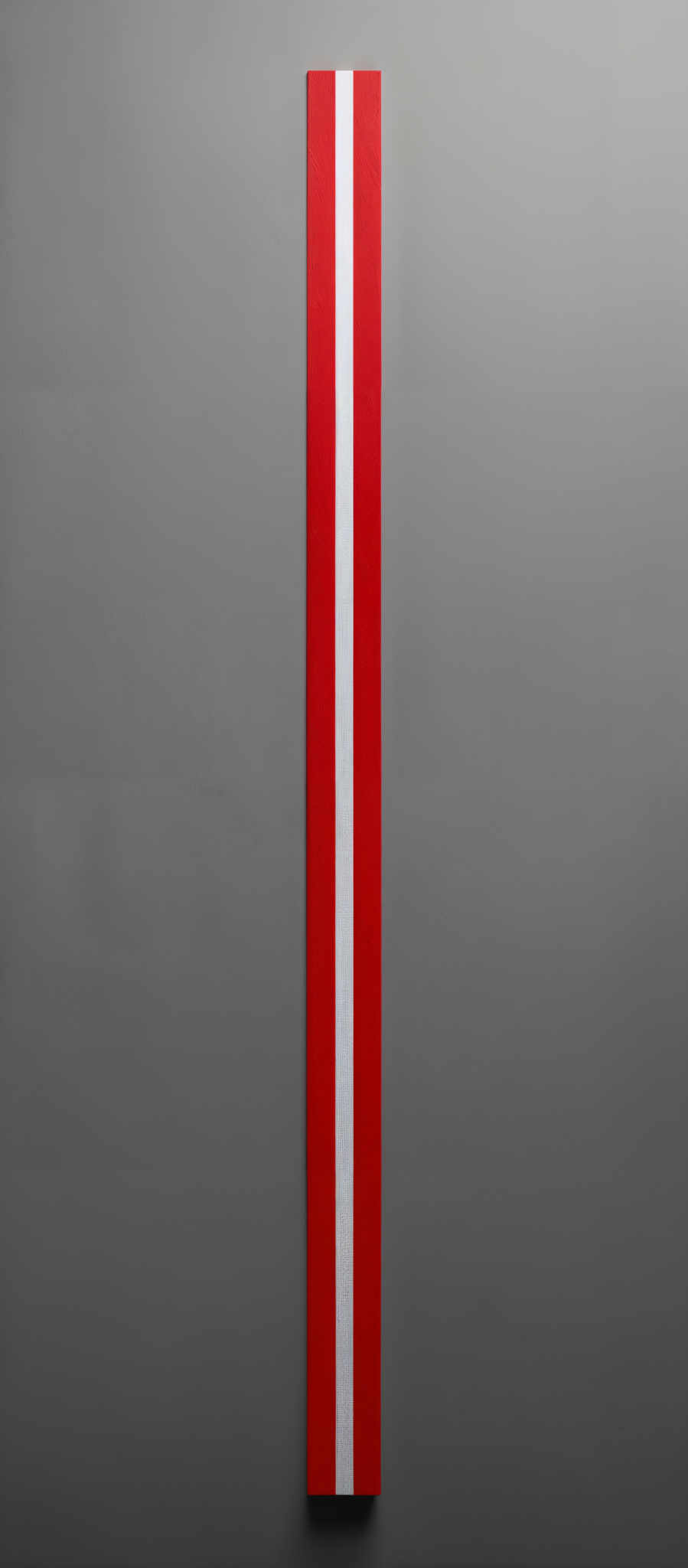 The image showcases a vertical rectangular object with a vibrant red background. There is a thin, white vertical stripe running through the center of the object. The background appears to be a muted gray, providing a contrast to the red and white.