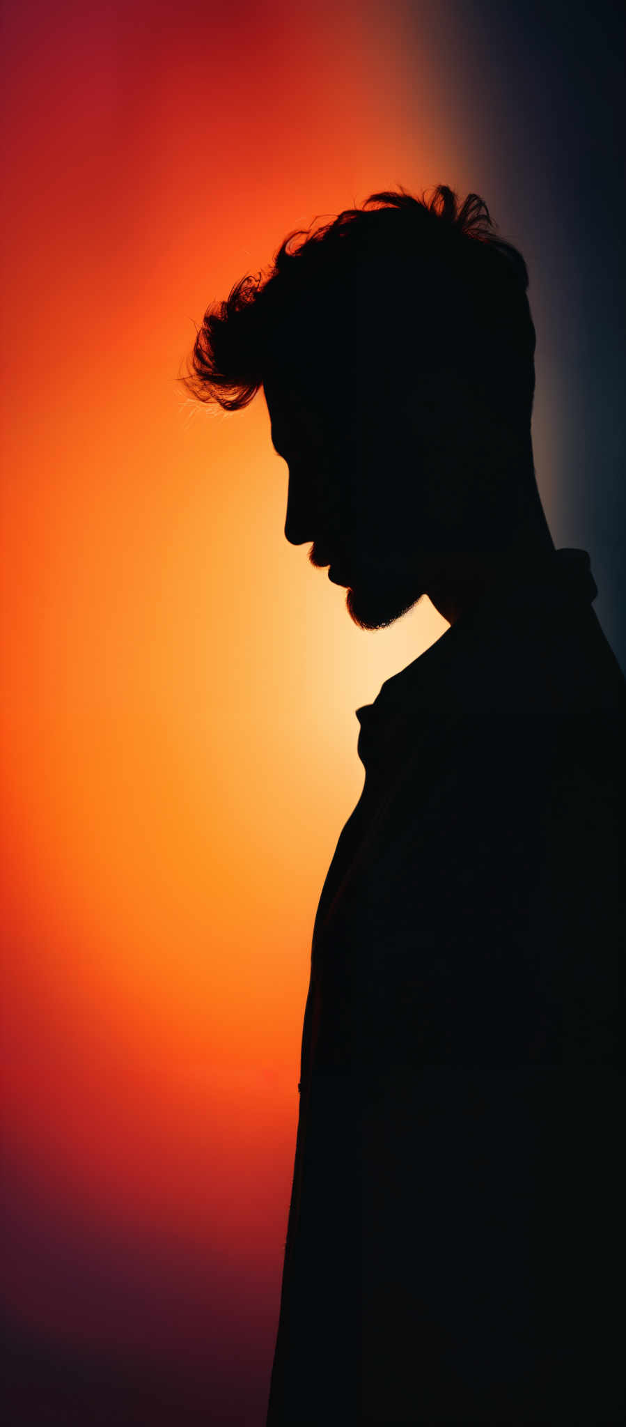 The image showcases a silhouette of a person's side profile against a gradient background. The background transitions from a deep red at the top to a warm orange at the bottom. The silhouetted figure appears to be a male with a distinctive hairstyle, featuring a raised tuft or quiff at the front. The person' has a beard and is wearing a collared shirt. The overall mood of the image is contemplative and serene, accentuated by the warm hues of the background.