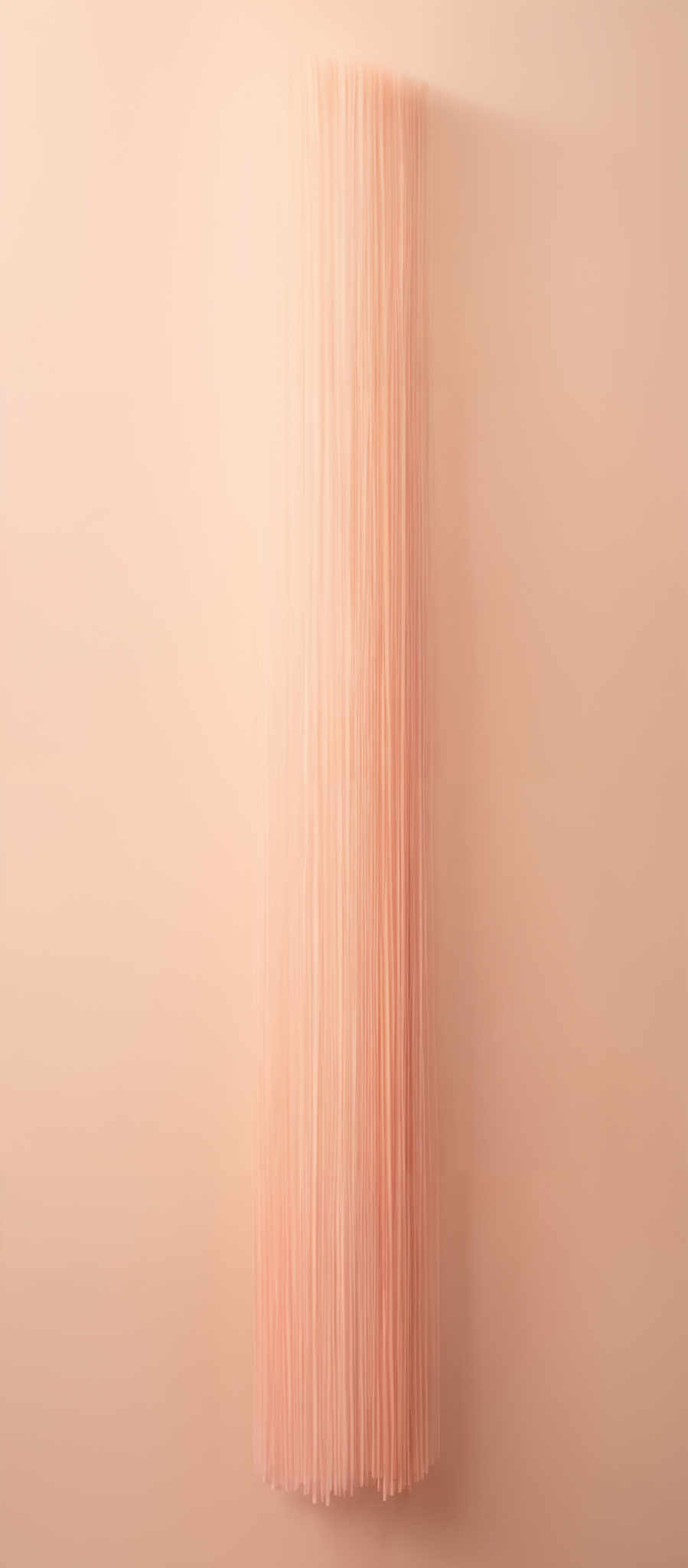 The image showcases a vertical cylindrical object with numerous thin strands or threads protruding from its surface. These strands are uniformly colored in a light beige or cream shade. The background is a solid beige color, creating a harmonious and minimalist aesthetic.