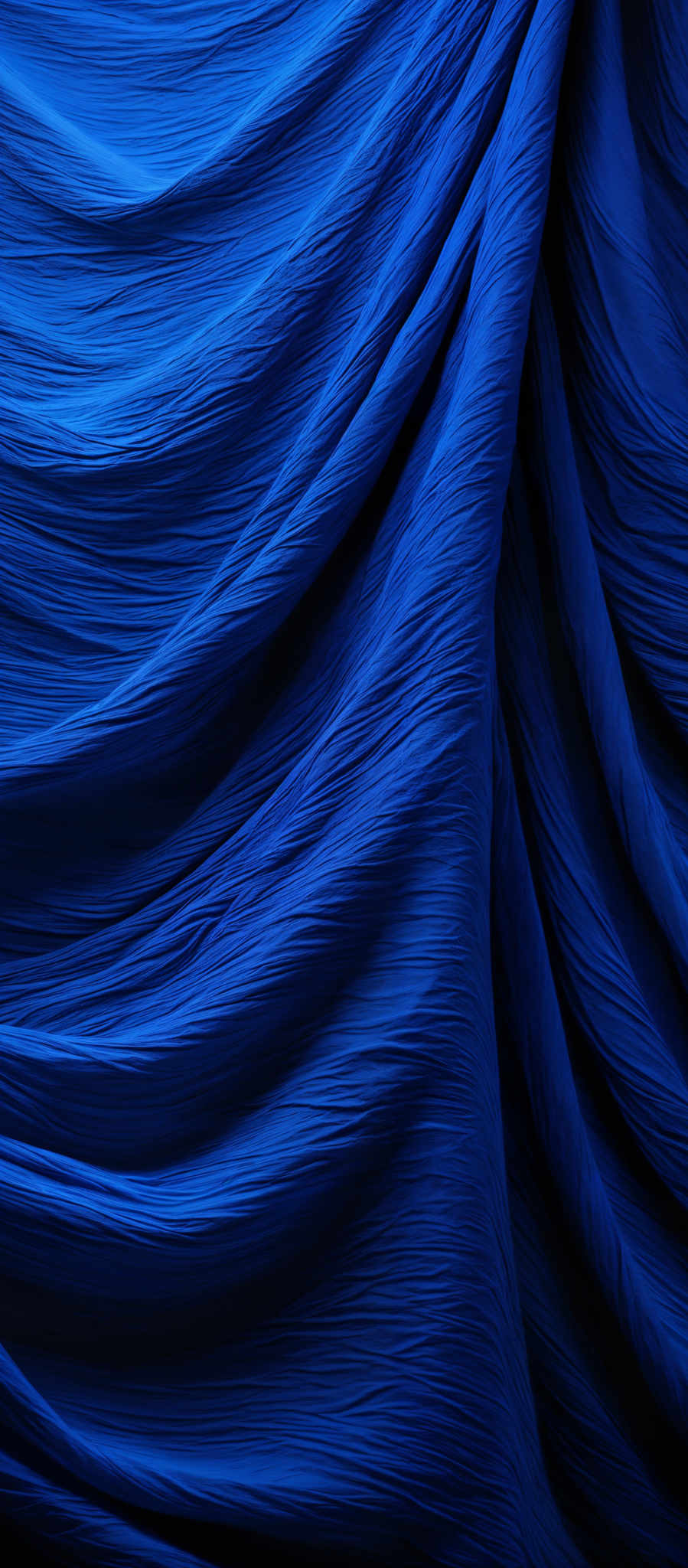 The image showcases a plethora of deep blue hues, with intricate folds and waves creating a textured appearance. The folds are layered and intertwined, creating a sense of depth and dimension. The color is consistent throughout, giving a serene and calming feel. The overall shape is reminiscent of flowing fabric or waves, suggesting movement and fluidity.