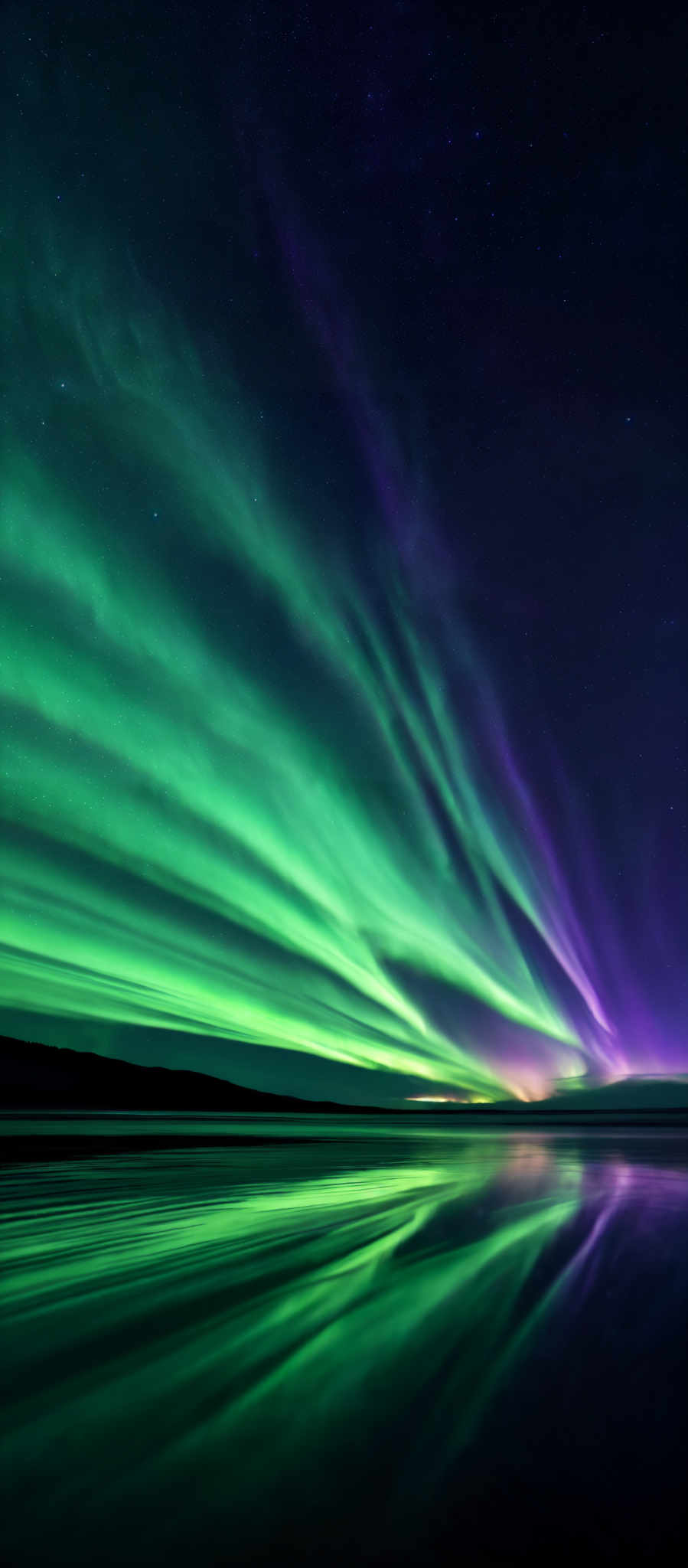 The image showcases a breathtaking view of the Northern Lights, also known as the Aurora Borealis. The colors are predominantly green and purple, with streaks of light cascading downwards. The shape is reminiscent of curtains or waves, flowing gracefully across the night sky. The Aurora is reflected beautifully on a calm body of water below, creating a mirrored effect. The backdrop is a starry night sky, adding to the ethereal beauty of the scene.