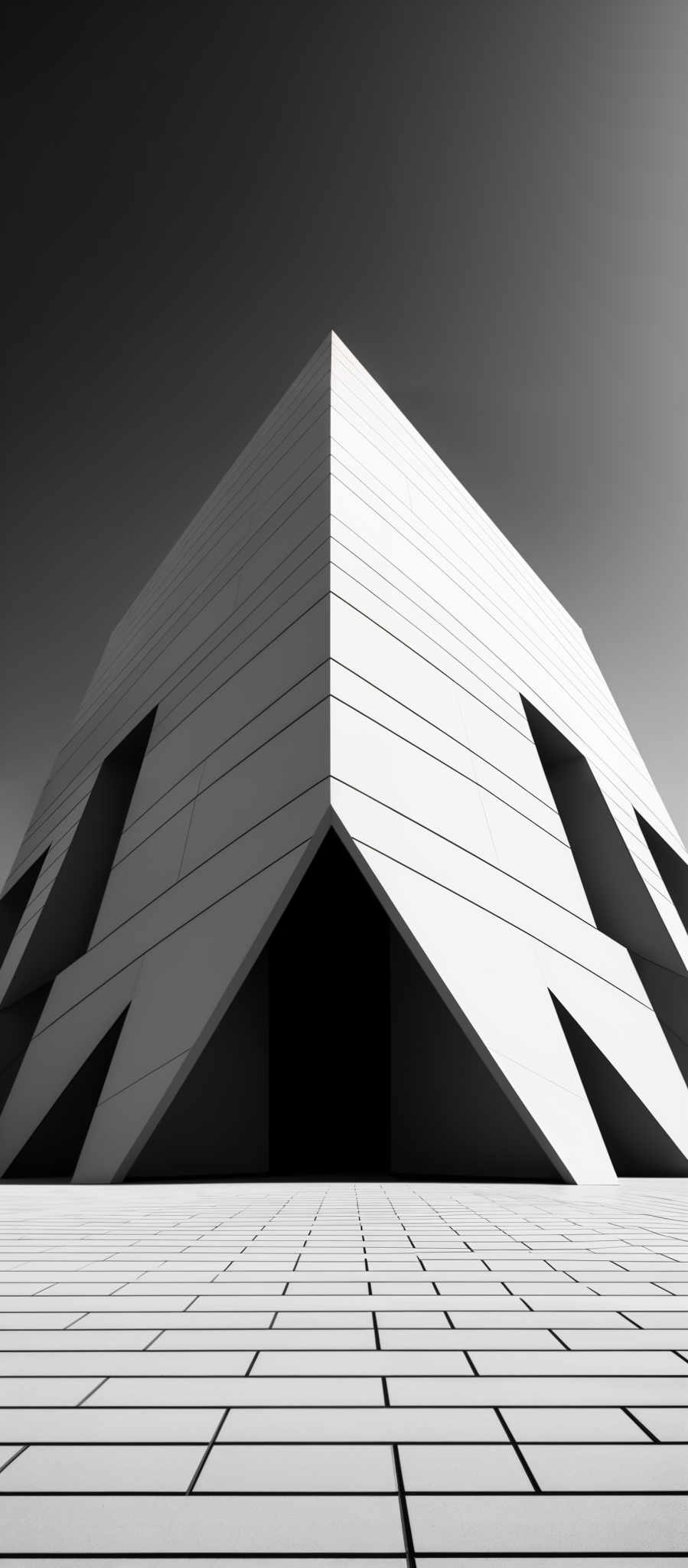 The image showcases a monochromatic architectural structure. The primary color is white, with the structure having a sharp, angular design. The building appears to have multiple geometric cutouts, creating a unique pattern on its facade. The ground is covered with a patterned tiled surface, which mirrors the design of the building, adding symmetry to the composition. The sky above is clear, providing a stark contrast to the dark openings in the building.