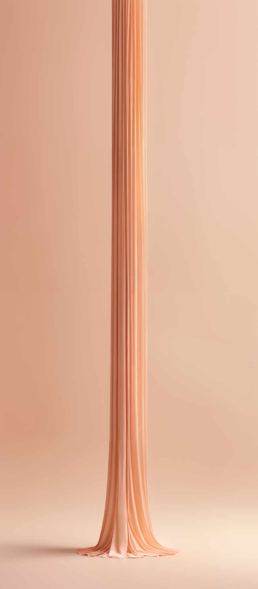 The image showcases a tall, vertical column of light peach or beige-colored fabric that appears to be draped or folded. The fabric has a smooth texture and cascades gracefully down to the floor, creating a soft fold at the base. The background is a muted beige, which complements the color of the fabric, creating an elegant and harmonious visual.