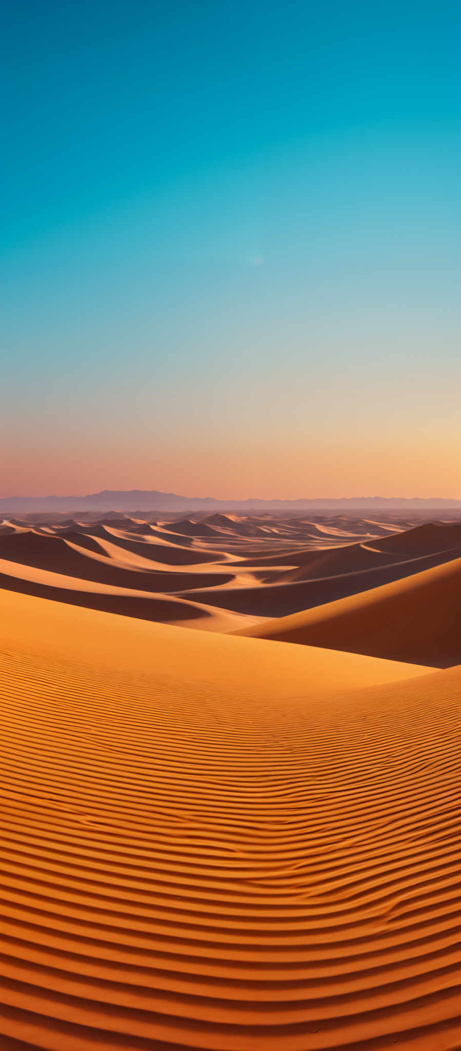 The image showcases a vast desert landscape with rolling sand dunes. The dominant color is a rich golden-orange, indicative of the sunlit sand. The dunes have a rippled texture, possibly caused by the wind. The sky above is clear with a gradient of colors, transitioning from a deep blue at the top to a soft pinkish hue near the horizon. In the distance, there are faint outlines of mountains or hills.