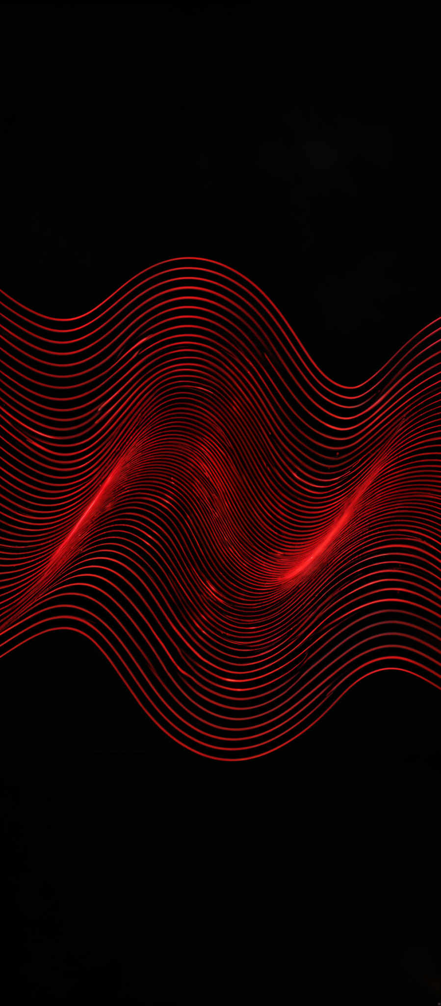 The image showcases a vibrant red color against a dark background. The primary shape is a series of interconnected, wavy lines that create a flowing, undulating pattern. These lines appear to be in motion, giving the image a dynamic and rhythmic feel. The interplay of light and shadow on the wavy patterns adds depth and dimension to the image, making it visually captivating.