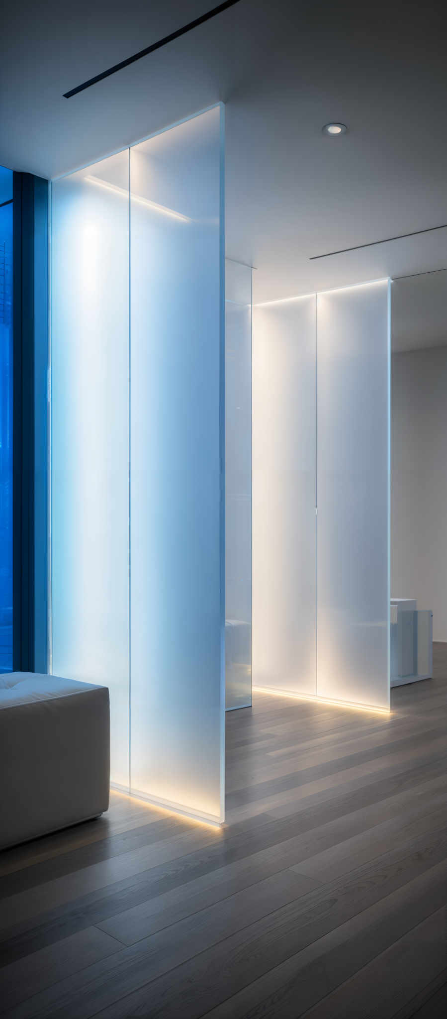 The image showcases a modern interior space with a predominantly neutral color palette. The primary colors are shades of white, gray, and brown. The room features tall, slender, and translucent partitions that are illuminated from within, casting a soft glow. These partitions are positioned in a way that they create distinct areas within the room, possibly serving as room dividers. The floor is made of wooden planks, and there's a large, square-shaped white bench or sofa near the window. The window itself offers a glimpse of a cityscape, suggesting that this space is located in an urban setting.